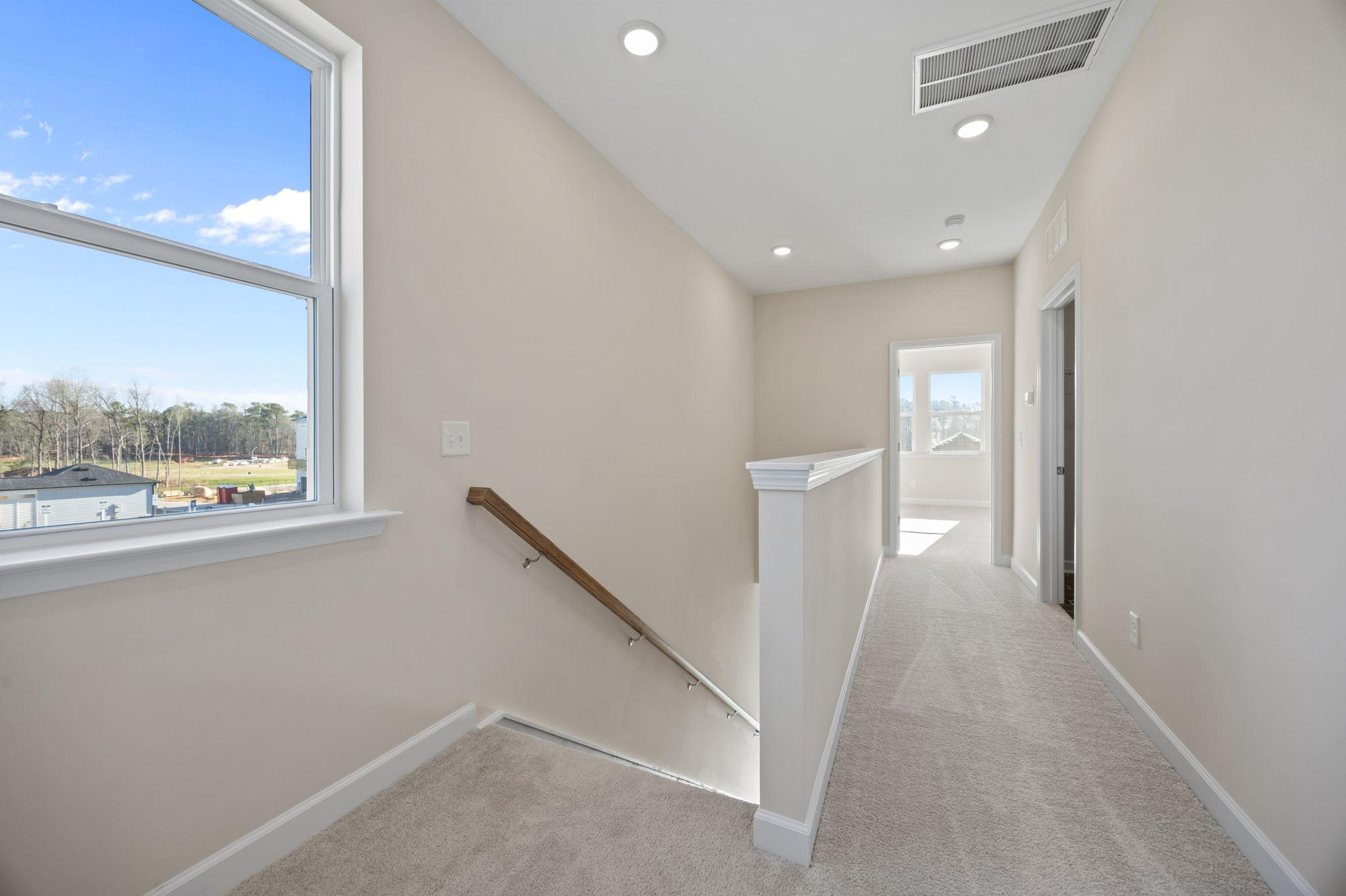 Bright second-floor hallway at Forestville Yard in Knightdale, NC by Davidson Homes with plush carpet and stair railing.