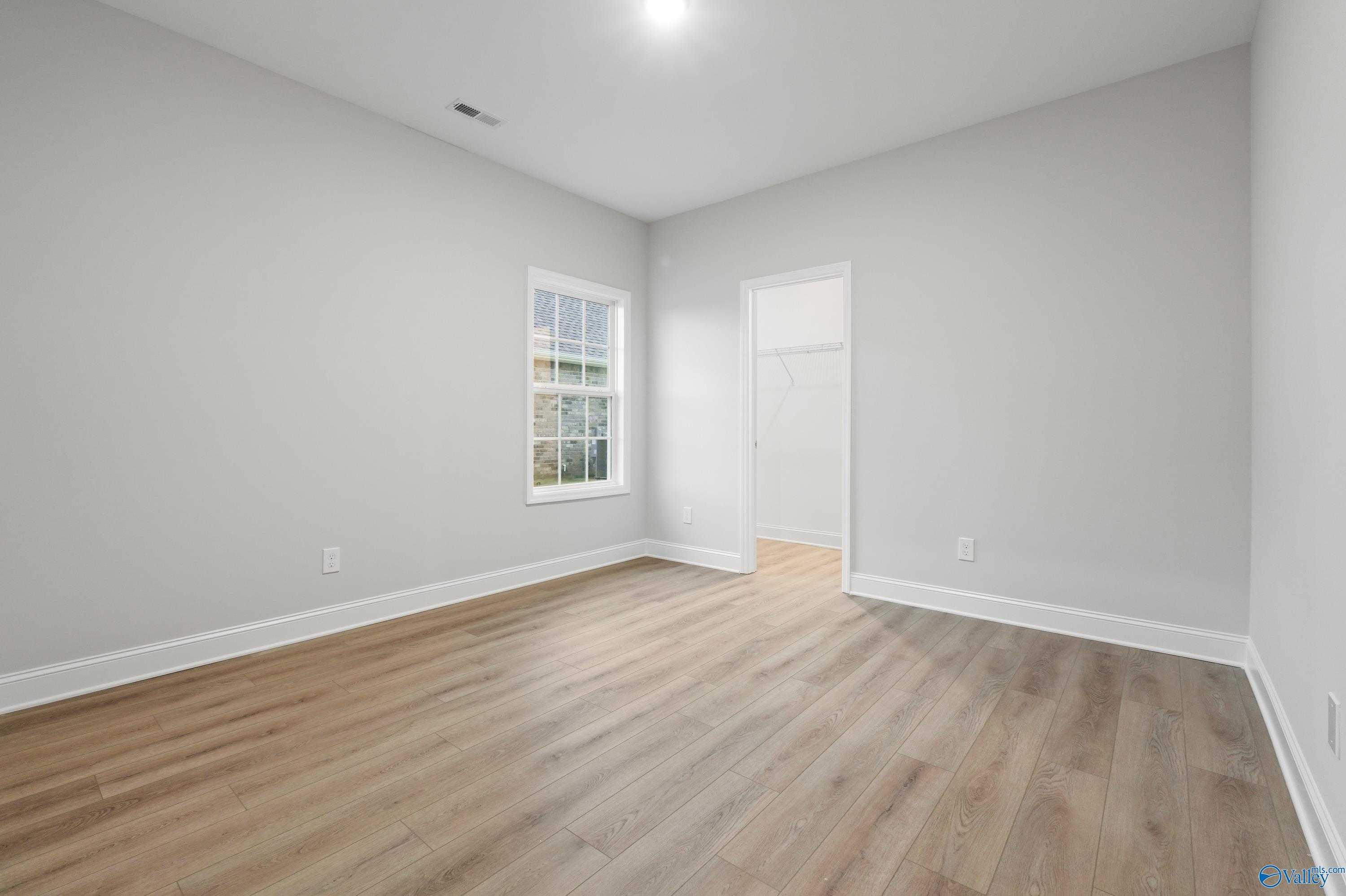 Bright secondary bedroom with light gray walls, hardwood floors, and large window in Davidson Homes The Lanier, Creekside Harvest AL