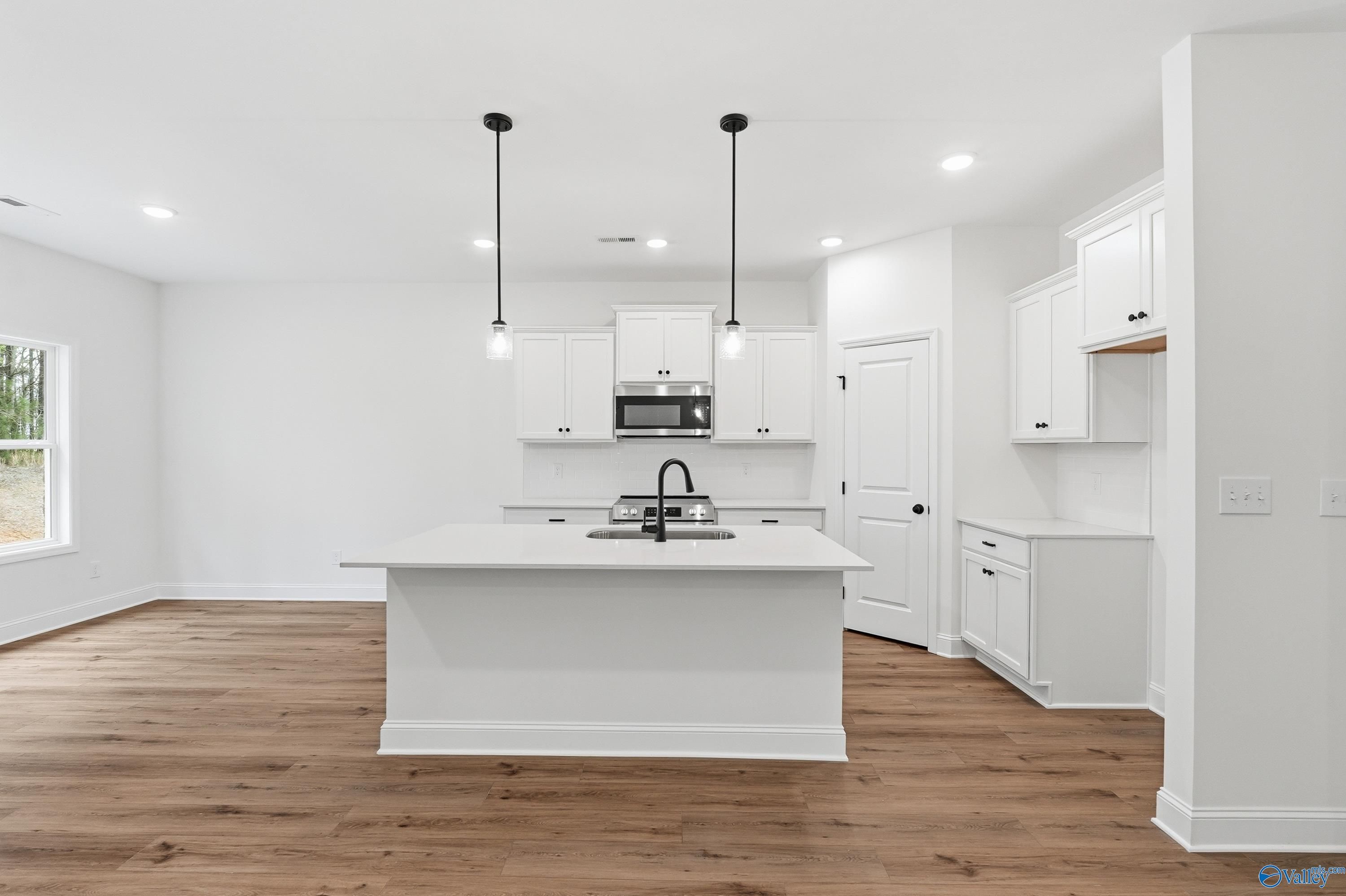 Modern white kitchen with central island sink, pendant lights, and hardwood floors in The Asheville C home, Arab, Alabama