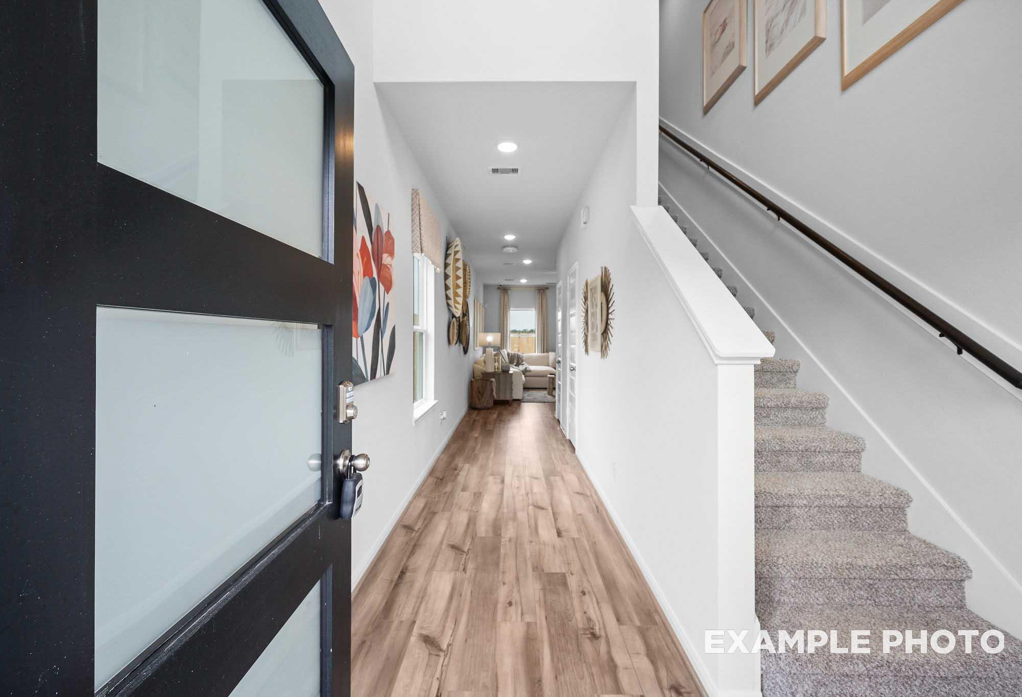 Spacious entry foyer in The Trinity floor plan featuring frosted glass door, hardwood floors, white walls, and carpeted staircase