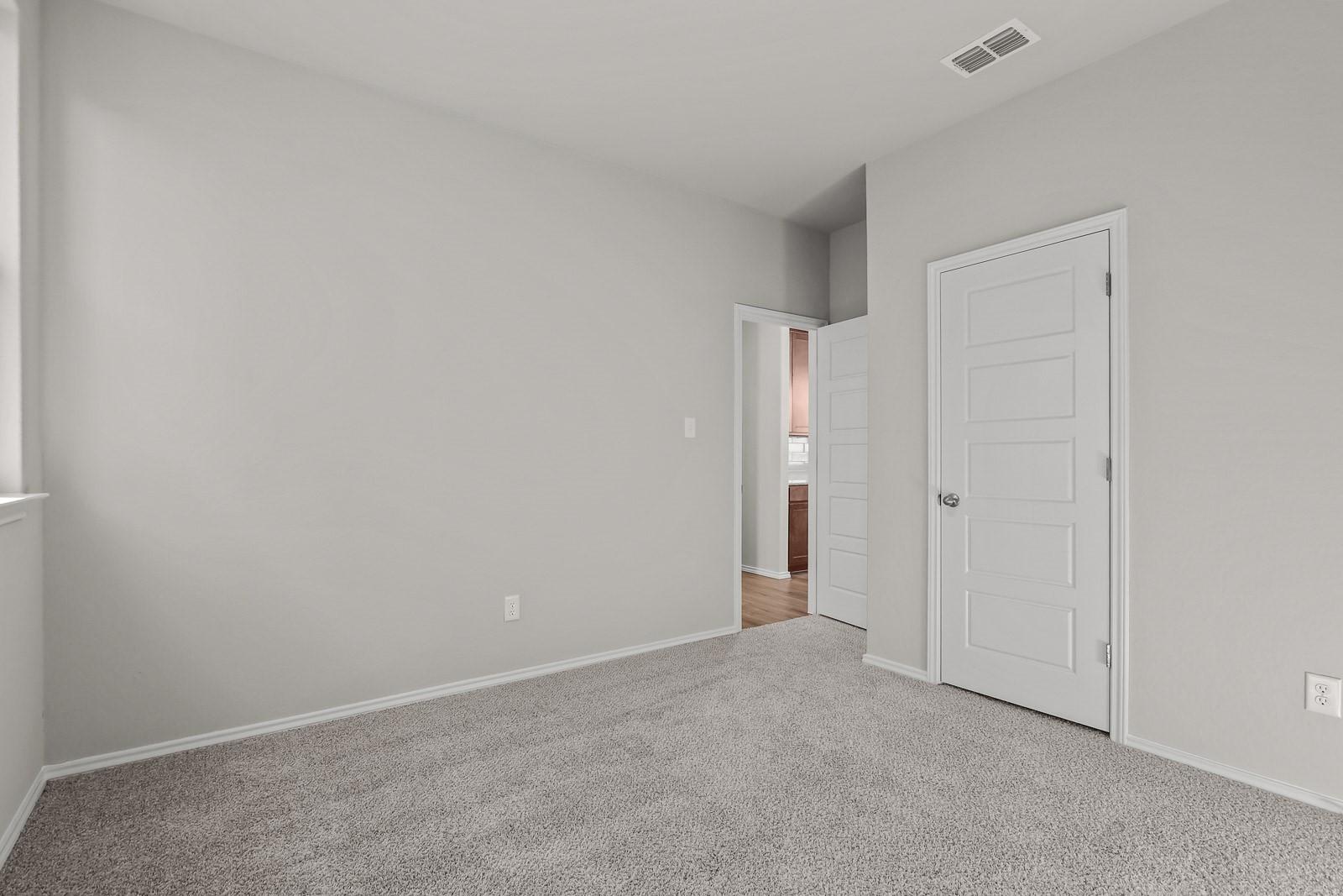 Spacious bedroom with neutral carpet and closet in The Frio G floor plan at Davidson Homes in Heartland, Texas.