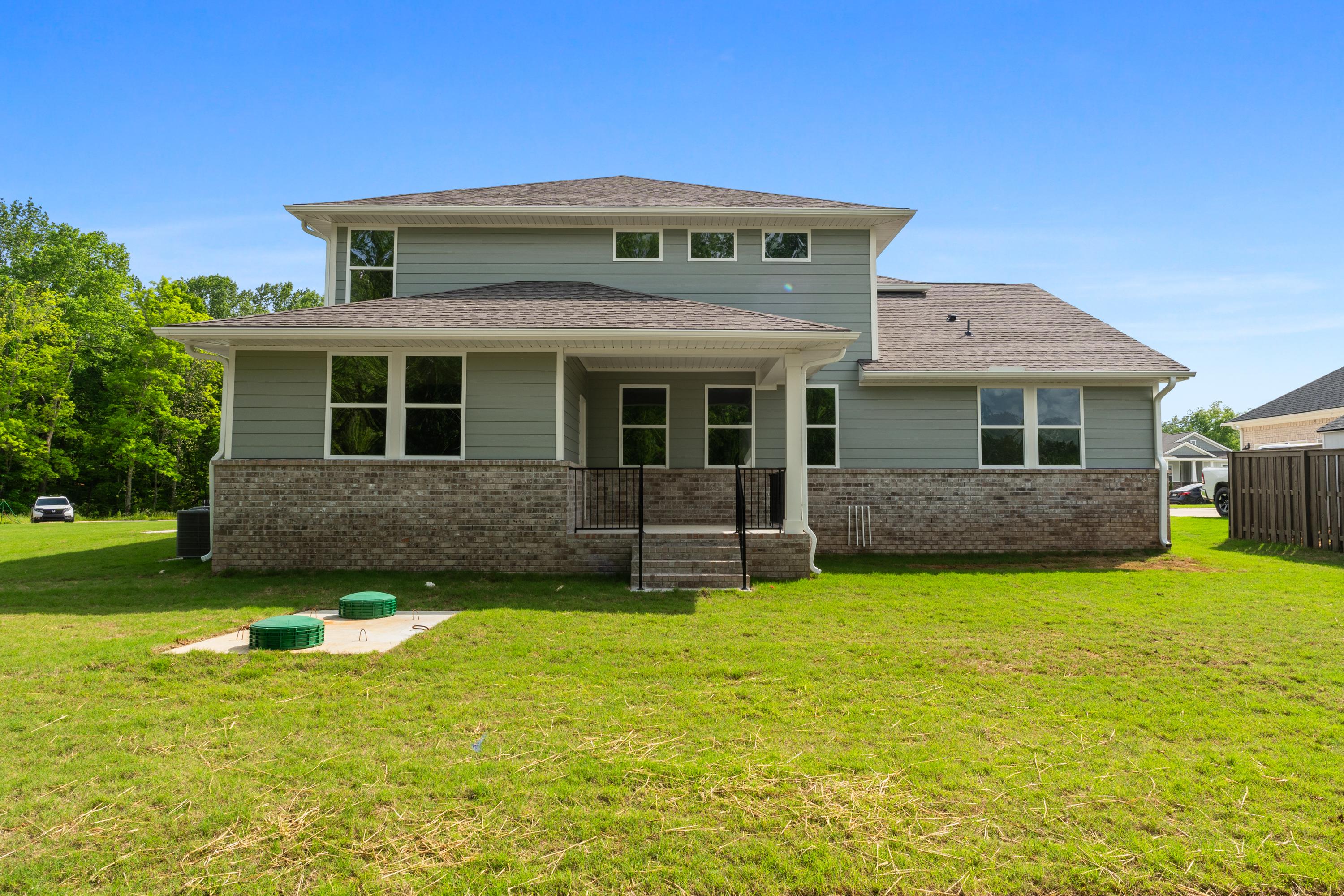 Rear elevation of The Avalon D two-story home with gray siding, brick accents, covered porch, large windows, and lush green yard in Owens Cross Roads