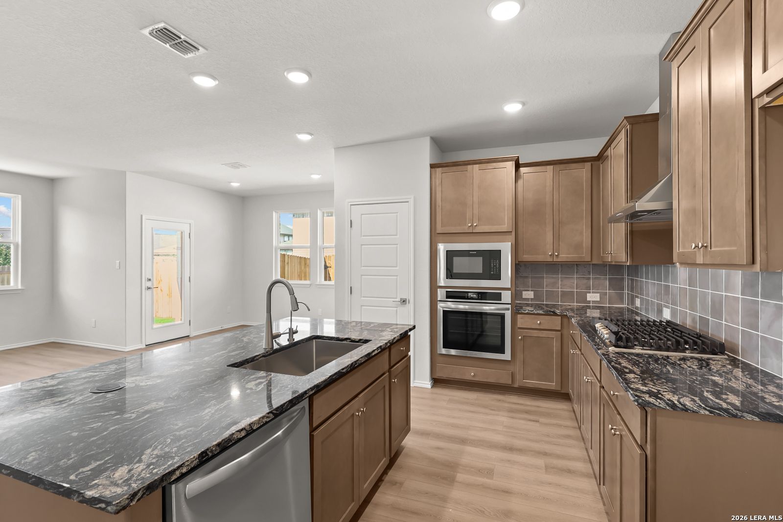 Kitchen with granite island, stainless appliances, and tile backsplash in Davidson Homes The Daphne I, Bricewood, San Antonio, Texas