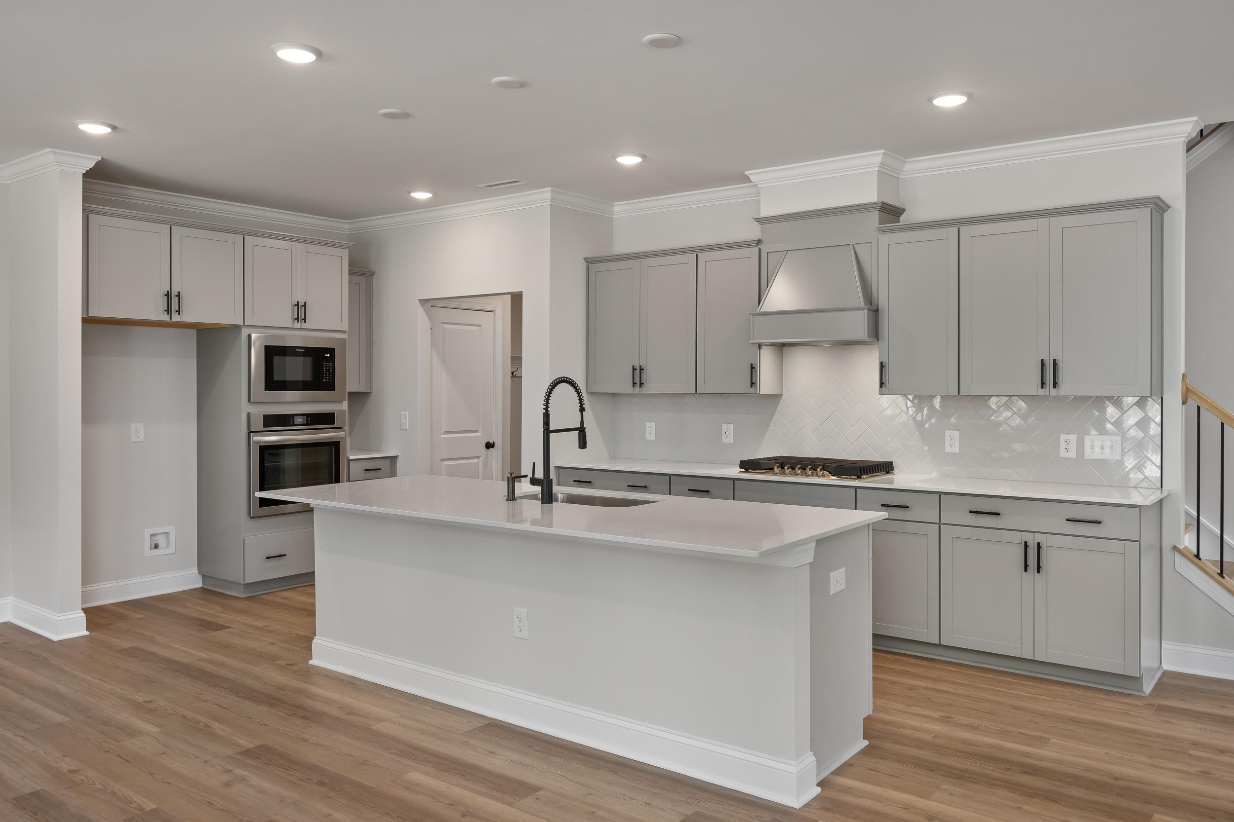 Spacious modern kitchen in The Beech A with gray shaker cabinets, white quartz island, gas cooktop, wall oven, and hardwood floors