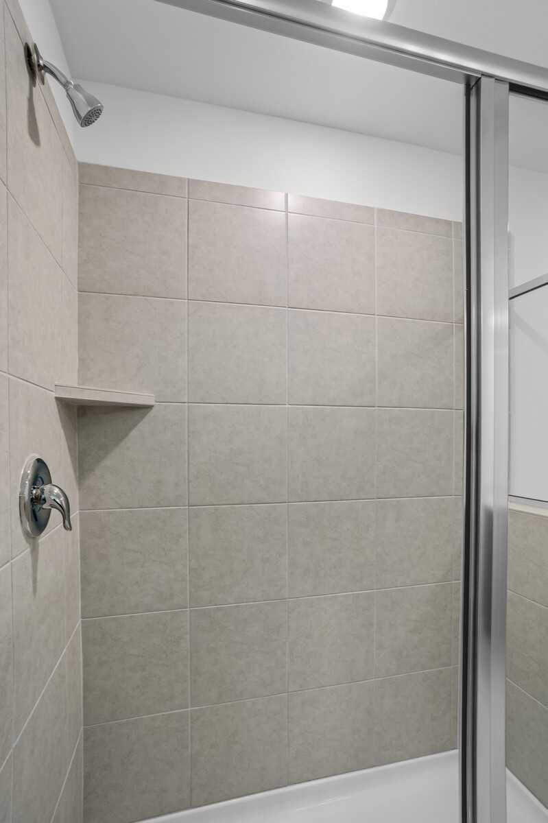 Modern walk-in shower with beige subway tiles, glass enclosure, and rainfall head in The Logan C master bath, White House TN