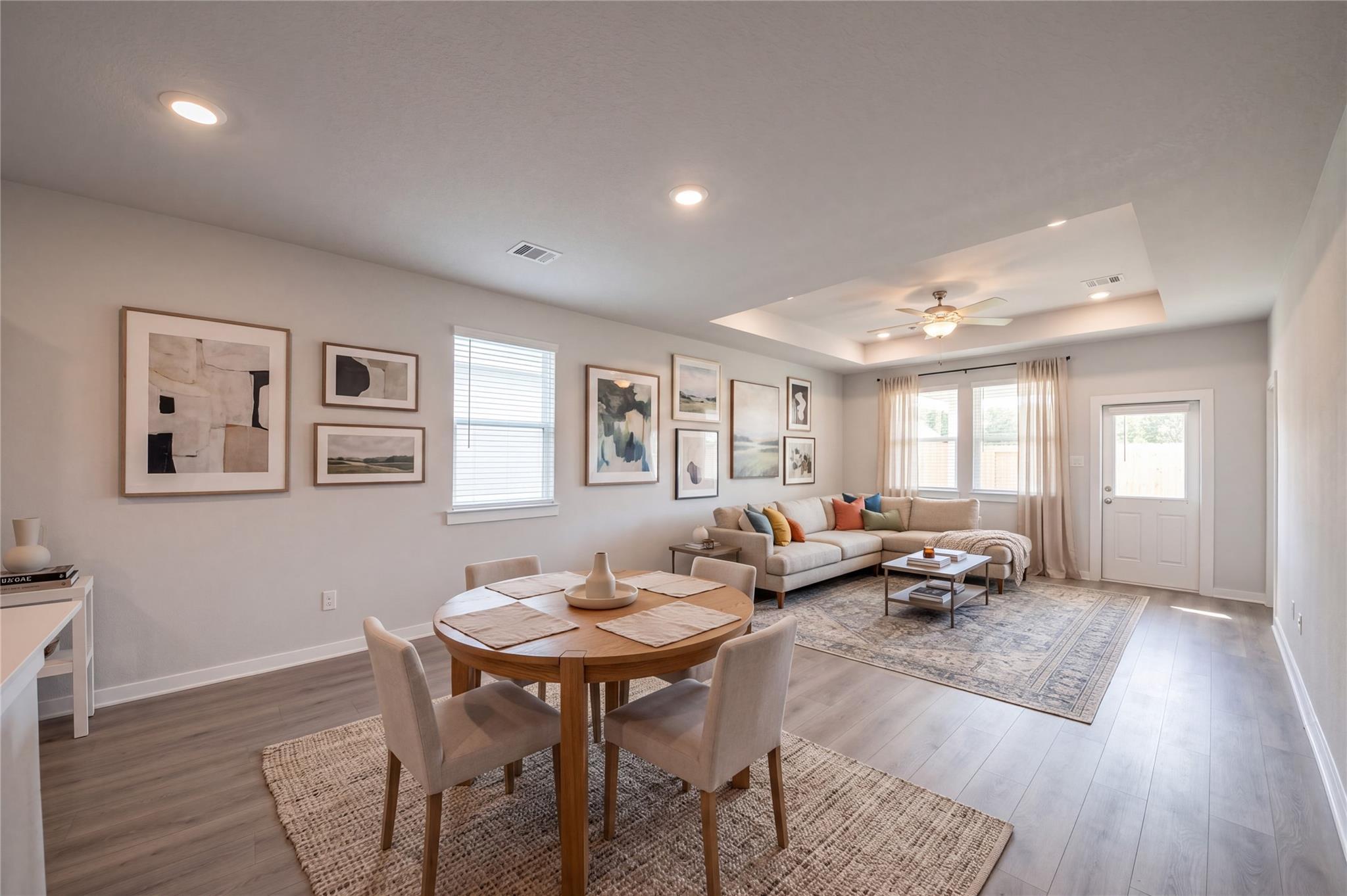 Open-concept dining and living area with tray ceiling and L-shaped sofa in Davidson Homes The Frio F, Cleveland, Texas