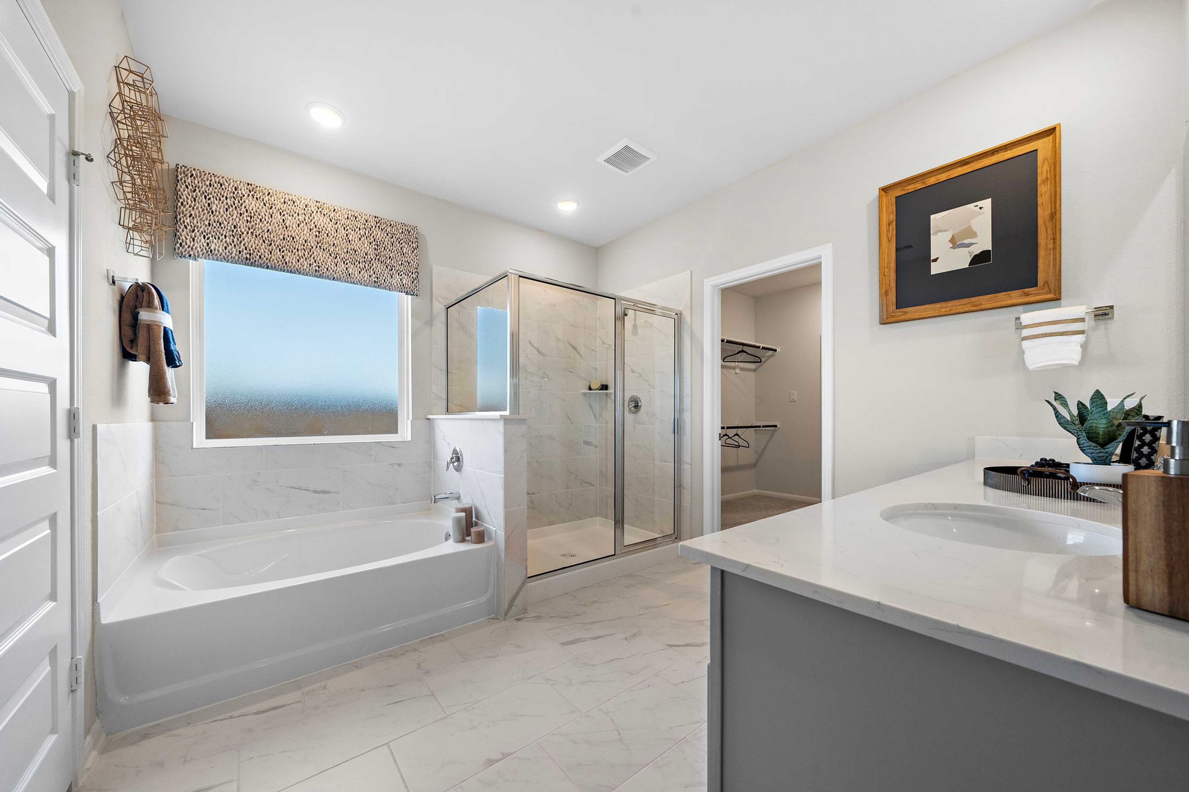Spacious master bathroom at Emberly in Beasley Texas with white bathtub glass shower marble vanity and scenic window view