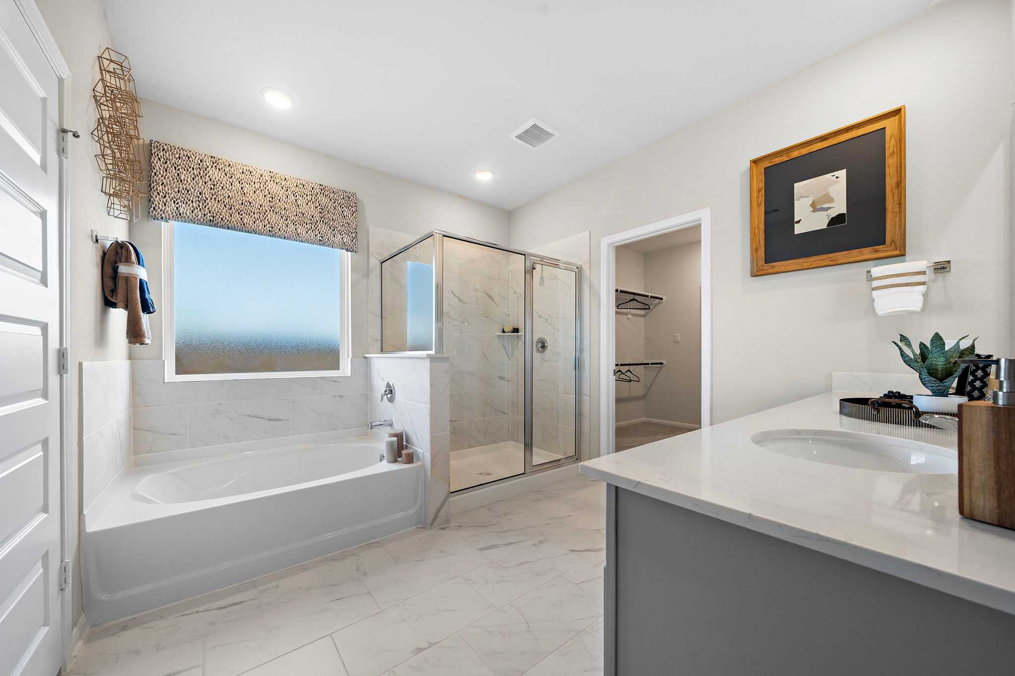 Spacious master bathroom at Emberly in Beasley Texas with white bathtub glass shower marble vanity and scenic window view