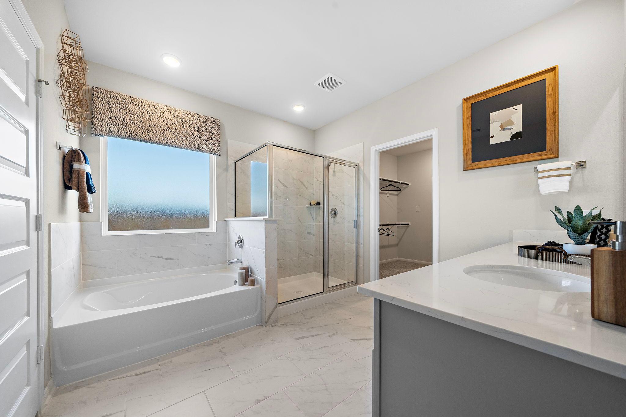 Spacious master bathroom at Emberly in Beasley Texas with white bathtub glass shower marble vanity and scenic window view