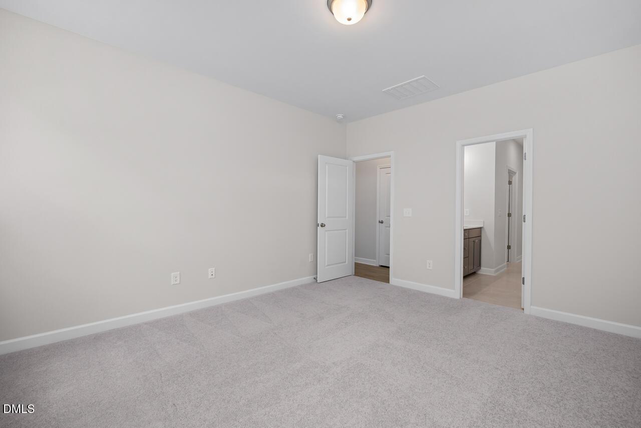 Spacious bedroom with plush carpet and en-suite bathroom in The Ashport G floor plan at Sage on North Main, Wake Forest.