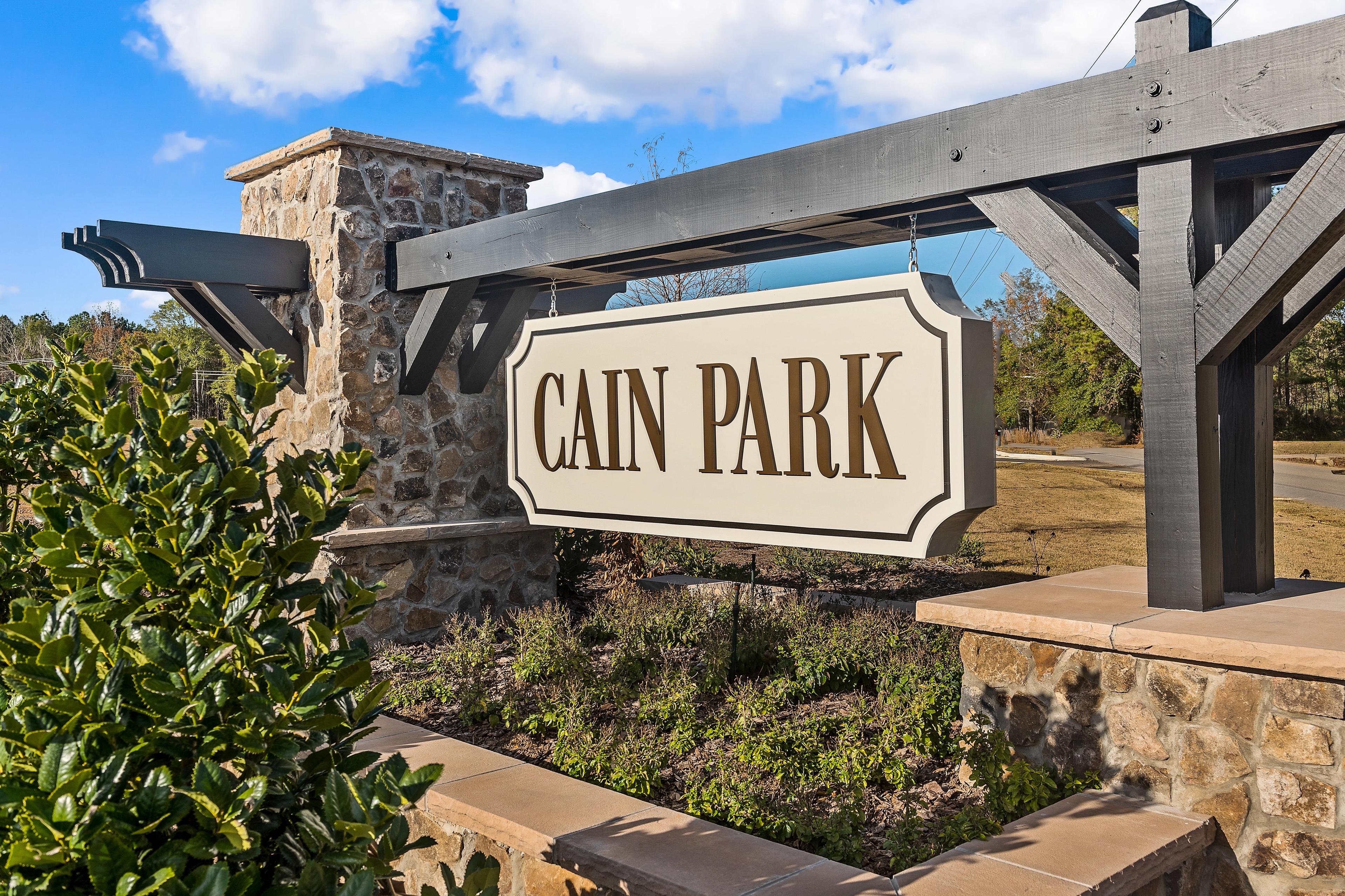 Cain Park entrance sign with stone pillars, wooden archway, green shrubs and blue sky in Hartselle Alabama