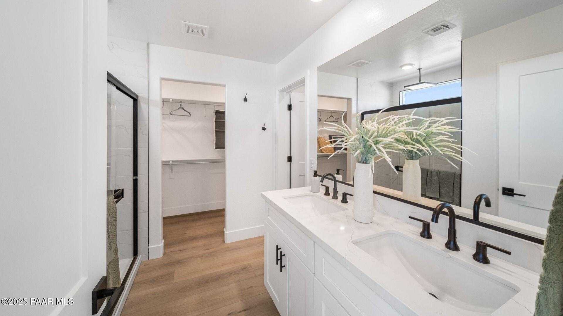 Modern master bathroom featuring double white vanity, black faucets, walk-in closet, and glass shower in Davidson Homes The Wilmington B, Prescott, AZ