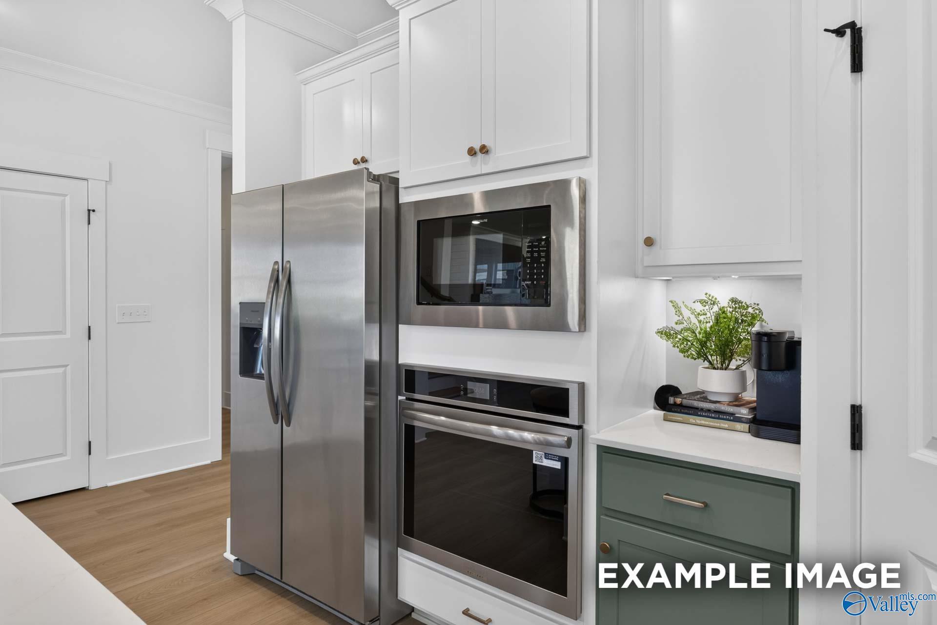 Modern kitchen with stainless steel appliances, white cabinetry, and sage green accents in Davidson Homes Ashport K, Hazel Green, Alabama
