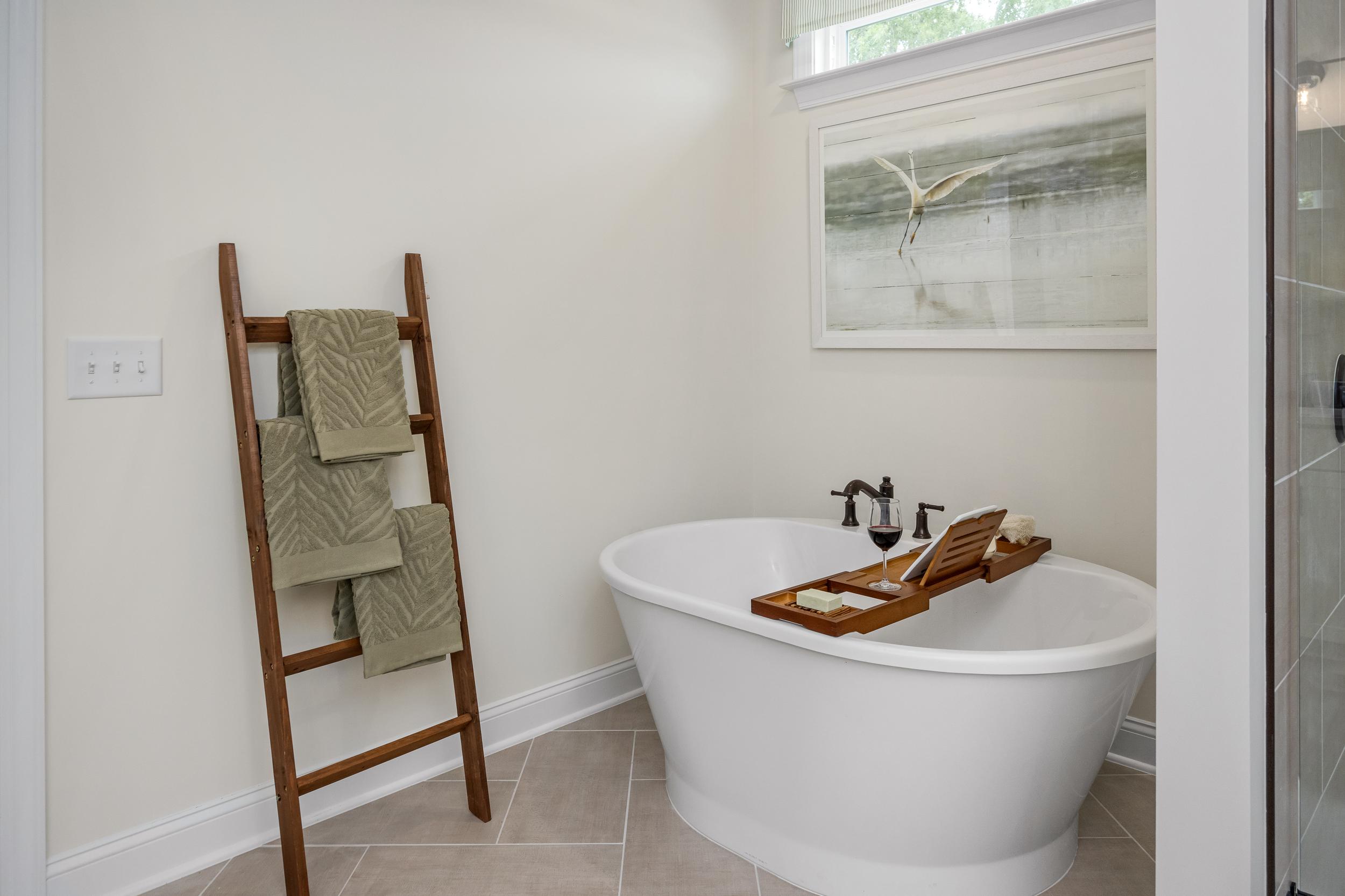 Elegant bathroom with freestanding white tub, green towels on wooden ladder, egret artwork at Laneridge Estates in Raleigh NC