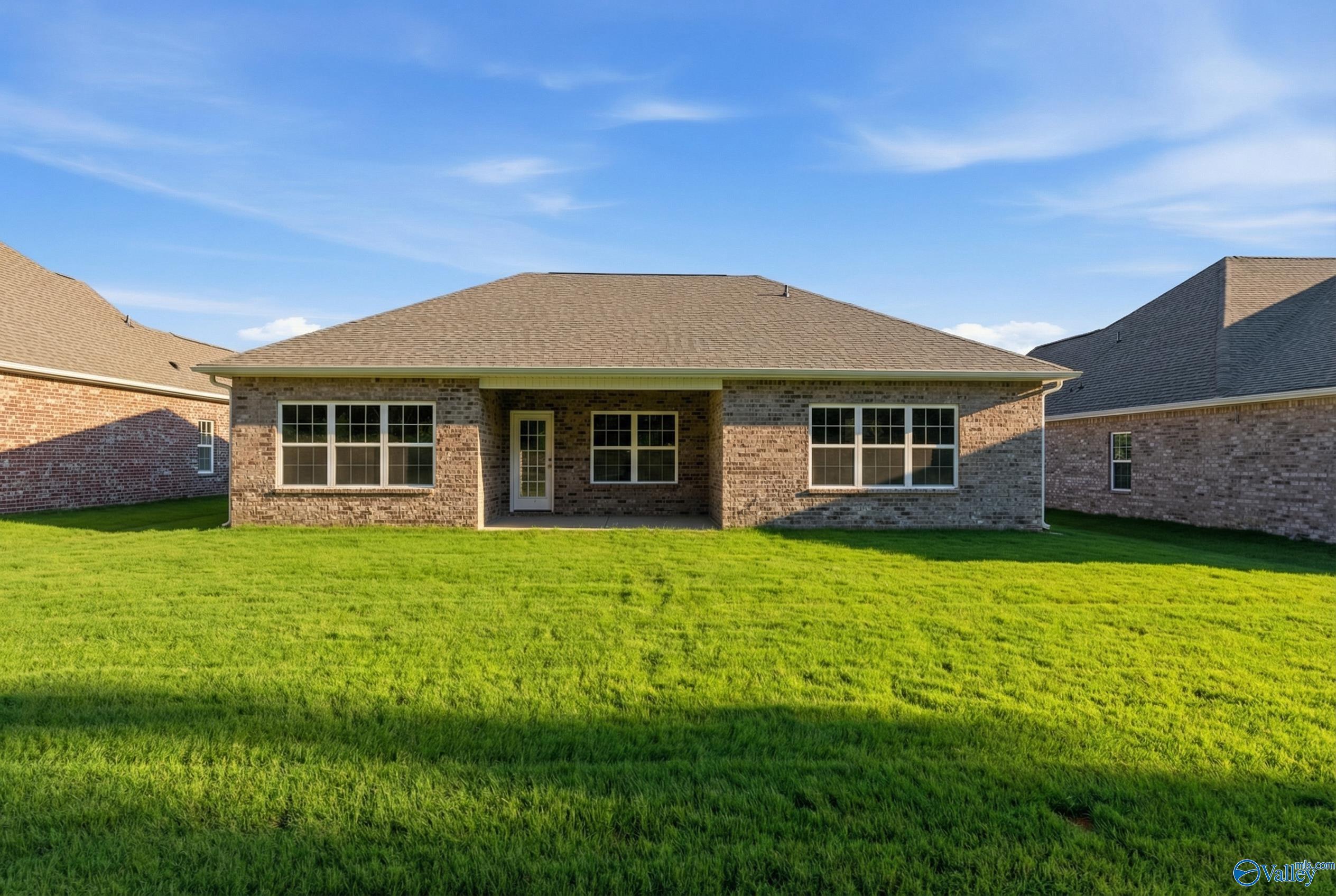 Rear brick exterior of Montgomery floor plan home with covered patio, large windows, and lush green lawn in Cain Park, Hartselle, Alabama