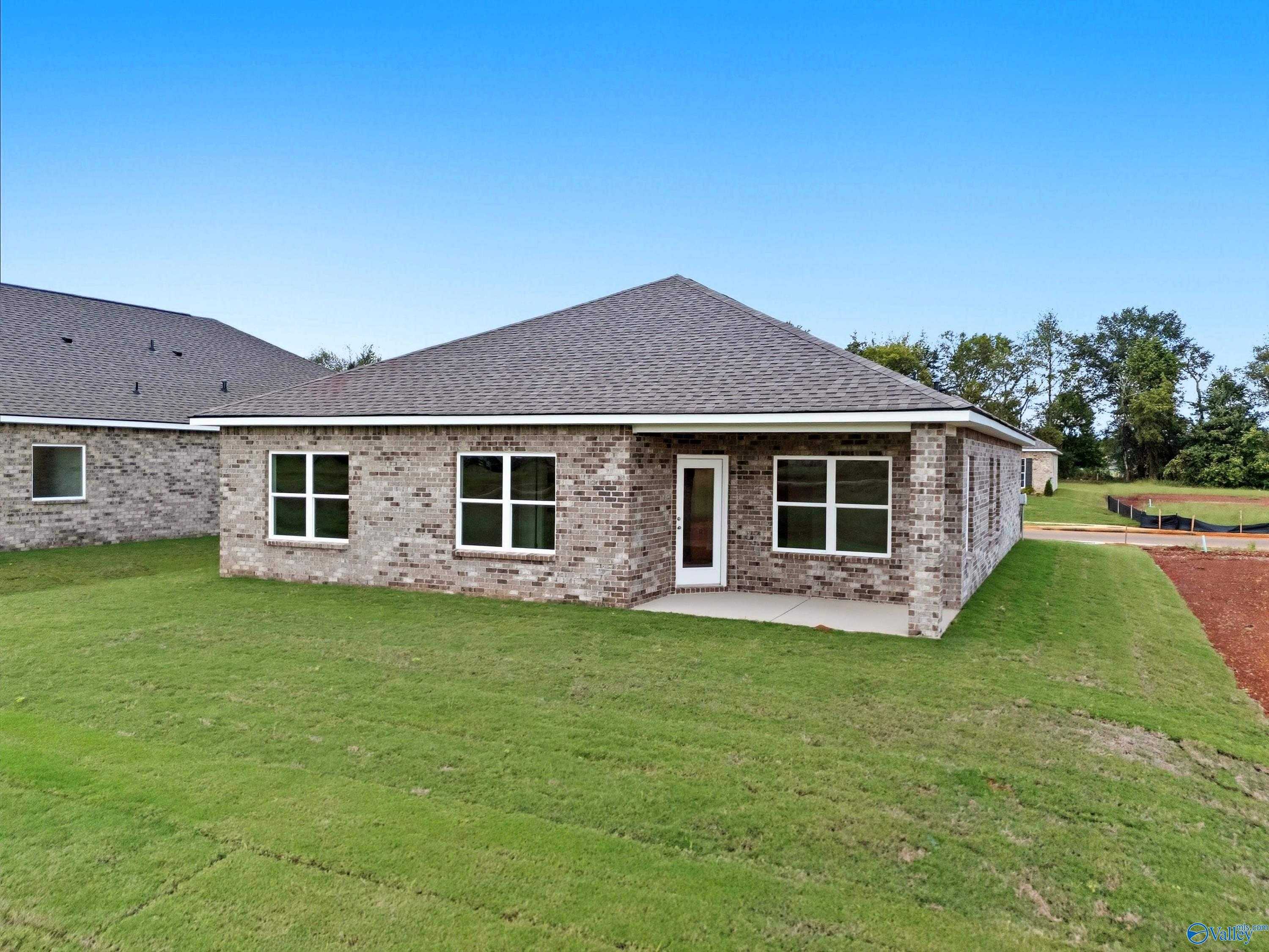 Single-story brick home exterior with covered porch, lush green yard, and blue sky in Lynn Meadows, Meridianville, Alabama - Davidson Homes The Franklin