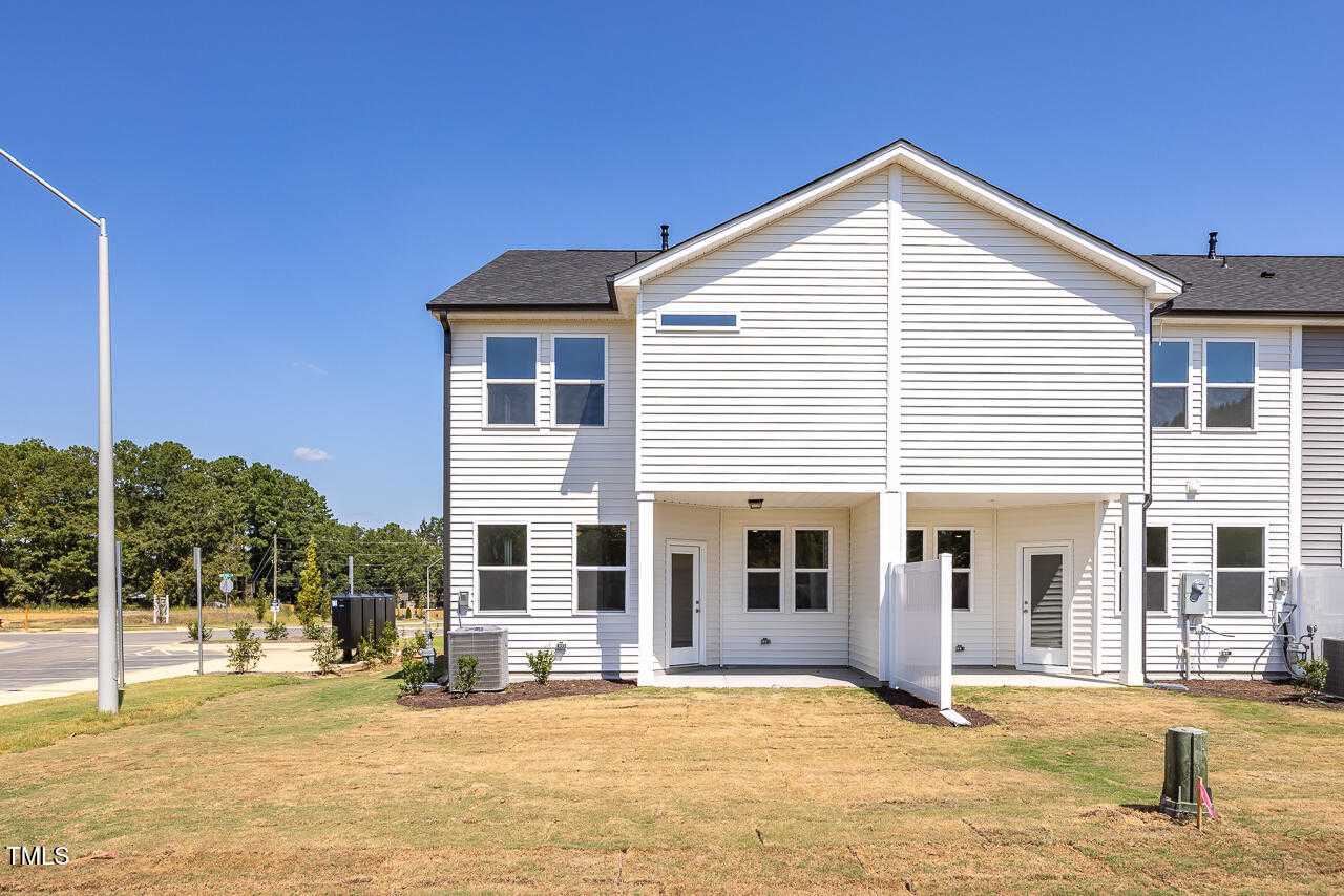 Rear view of The Graham Exterior two-story white home with covered patio, privacy fence, and grassy yard in Springvale, Fuquay-Varina
