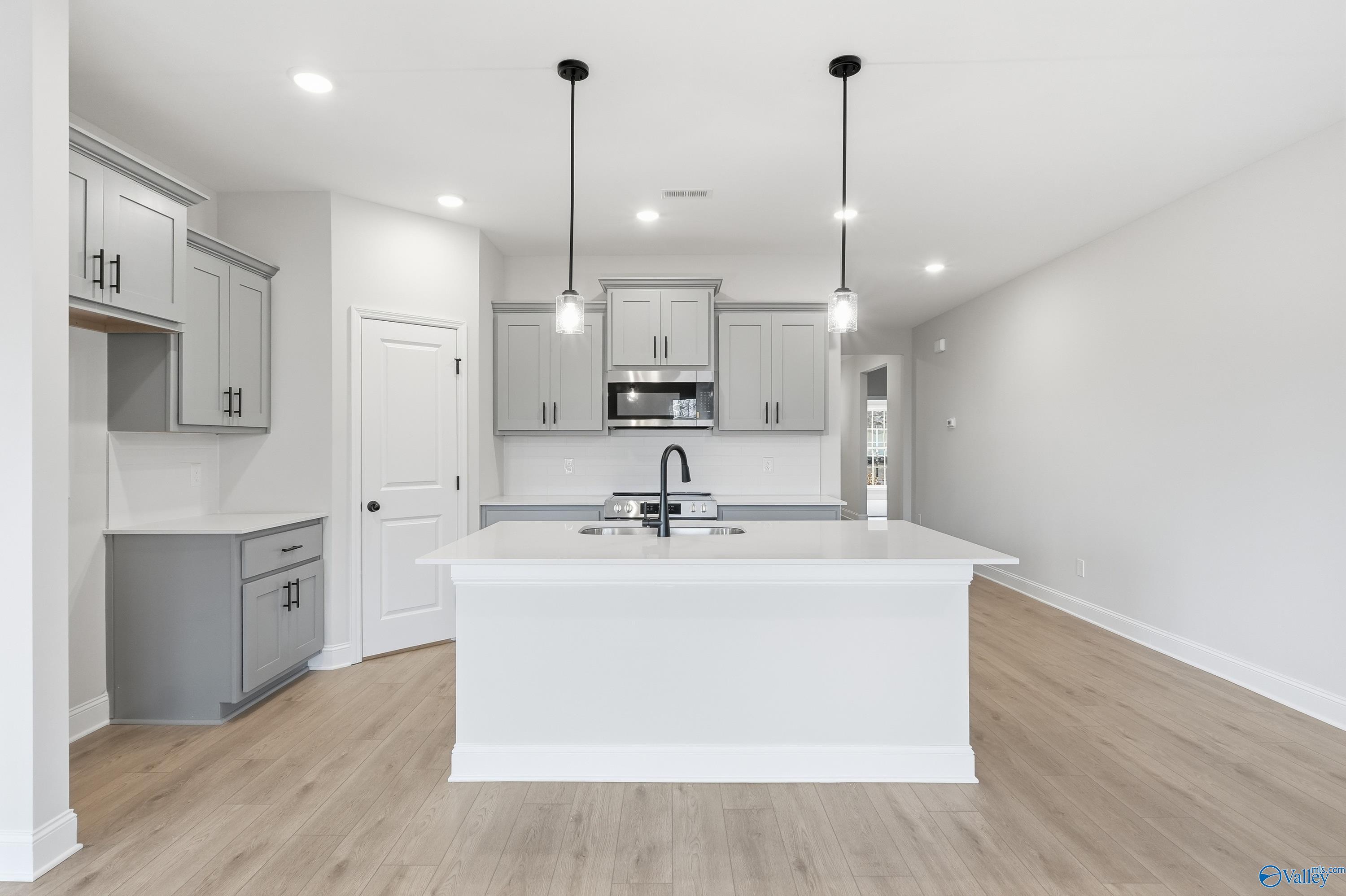 Modern kitchen with white quartz island, gray shaker cabinets, stainless appliances in Davidson Homes The Daphne C, Athens, AL