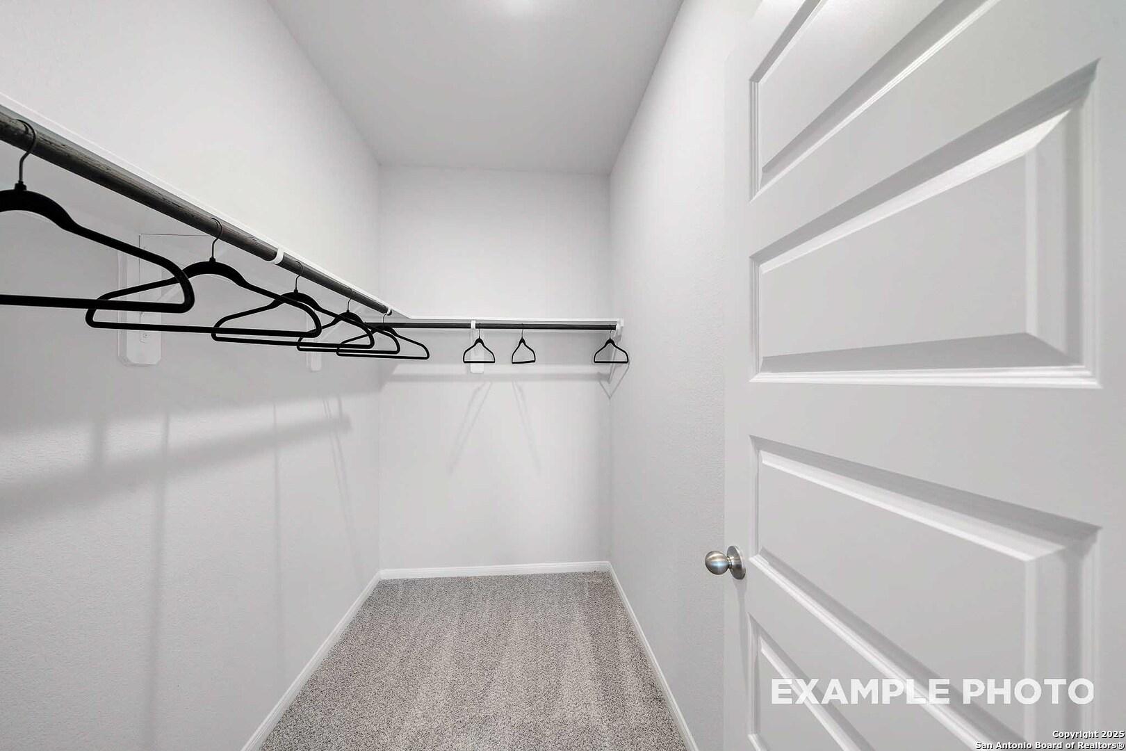 Spacious walk-in closet with black hanging rods and gray carpet in Davidson Homes The San Marcos D, San Antonio