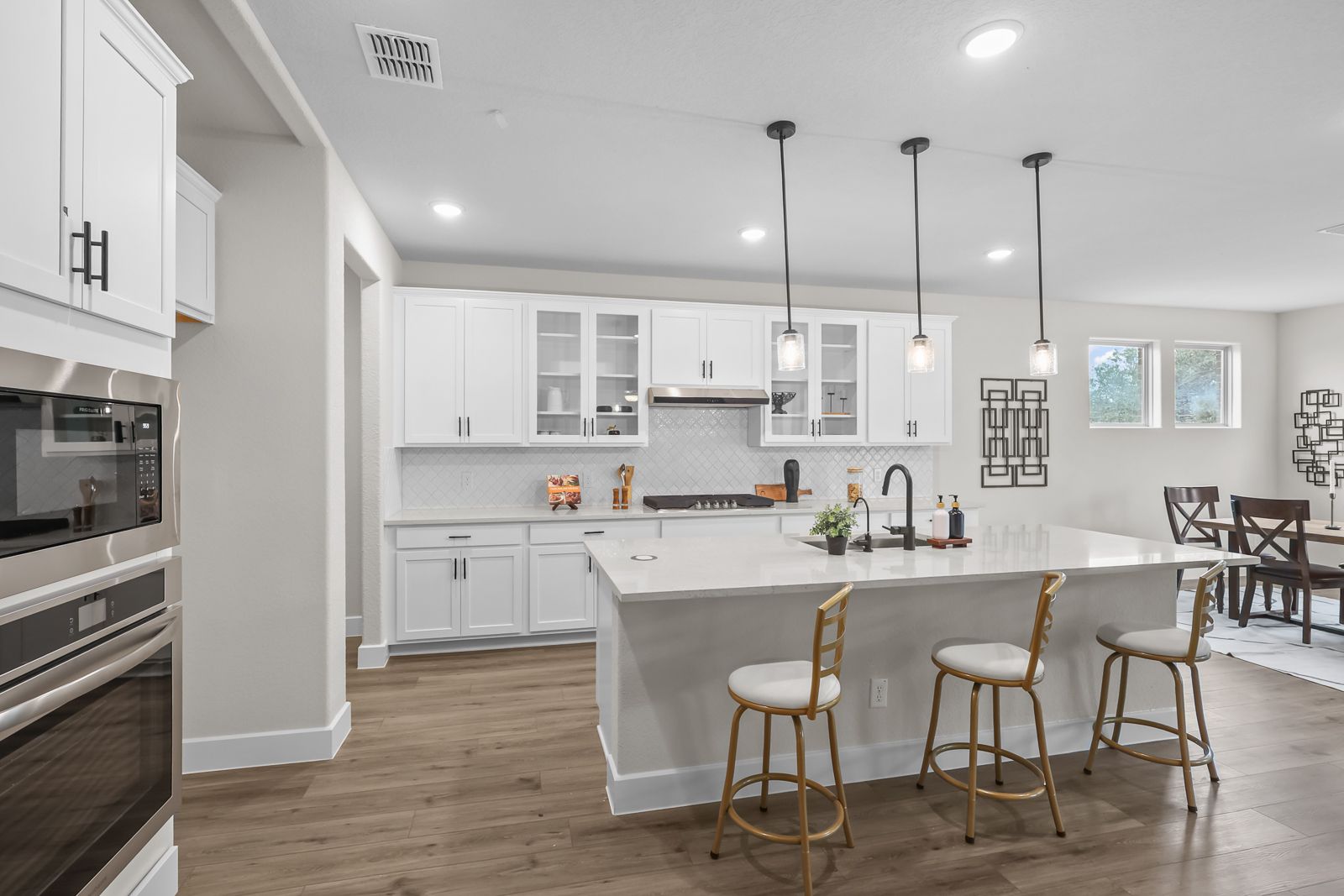 Modern white kitchen in The Belmont featuring a large island, stainless appliances, and open-concept dining area.