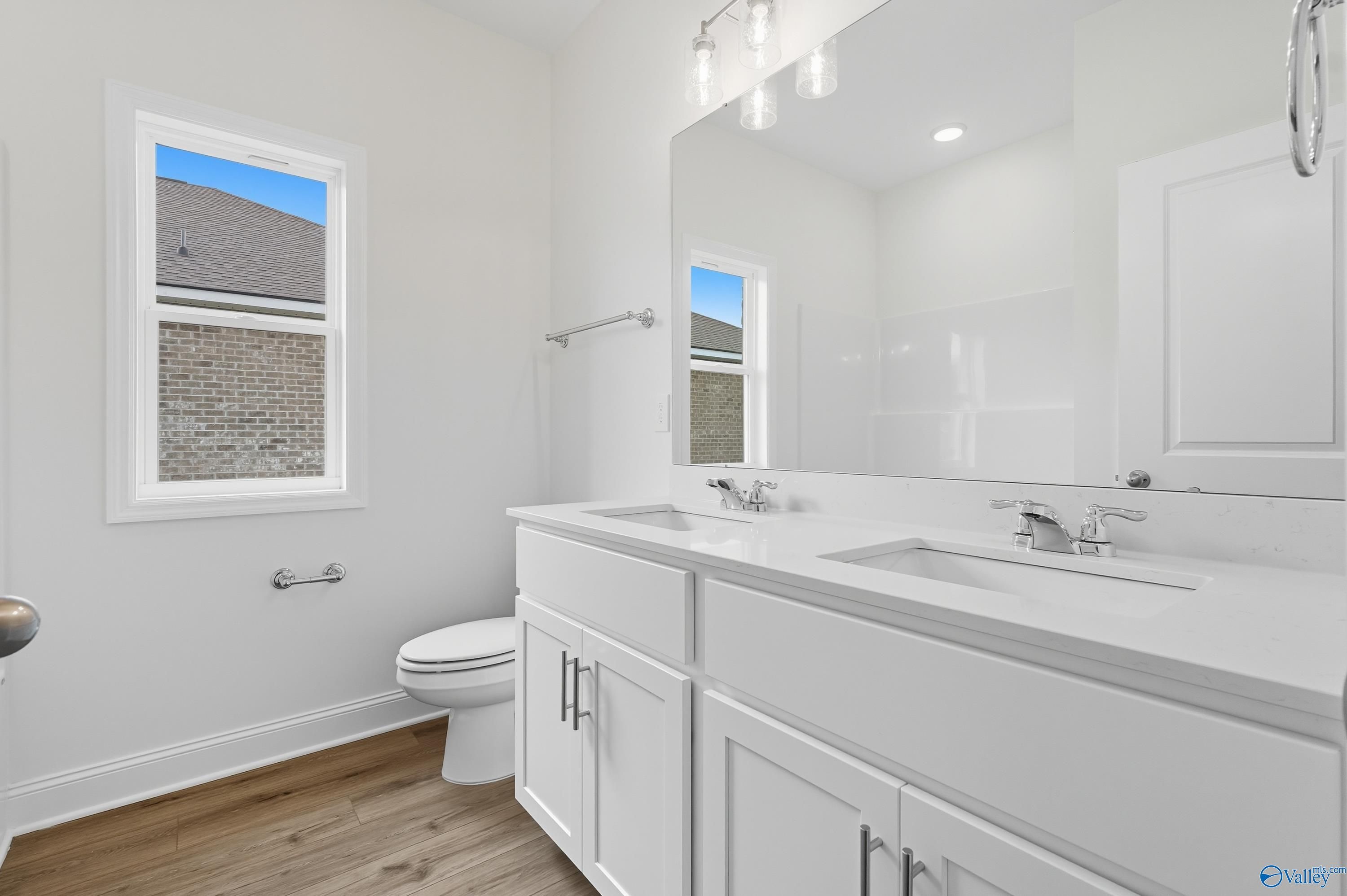 Modern double-sink vanity bathroom with white cabinets, large mirror, and window view in The Everett home, Meridianville, Alabama