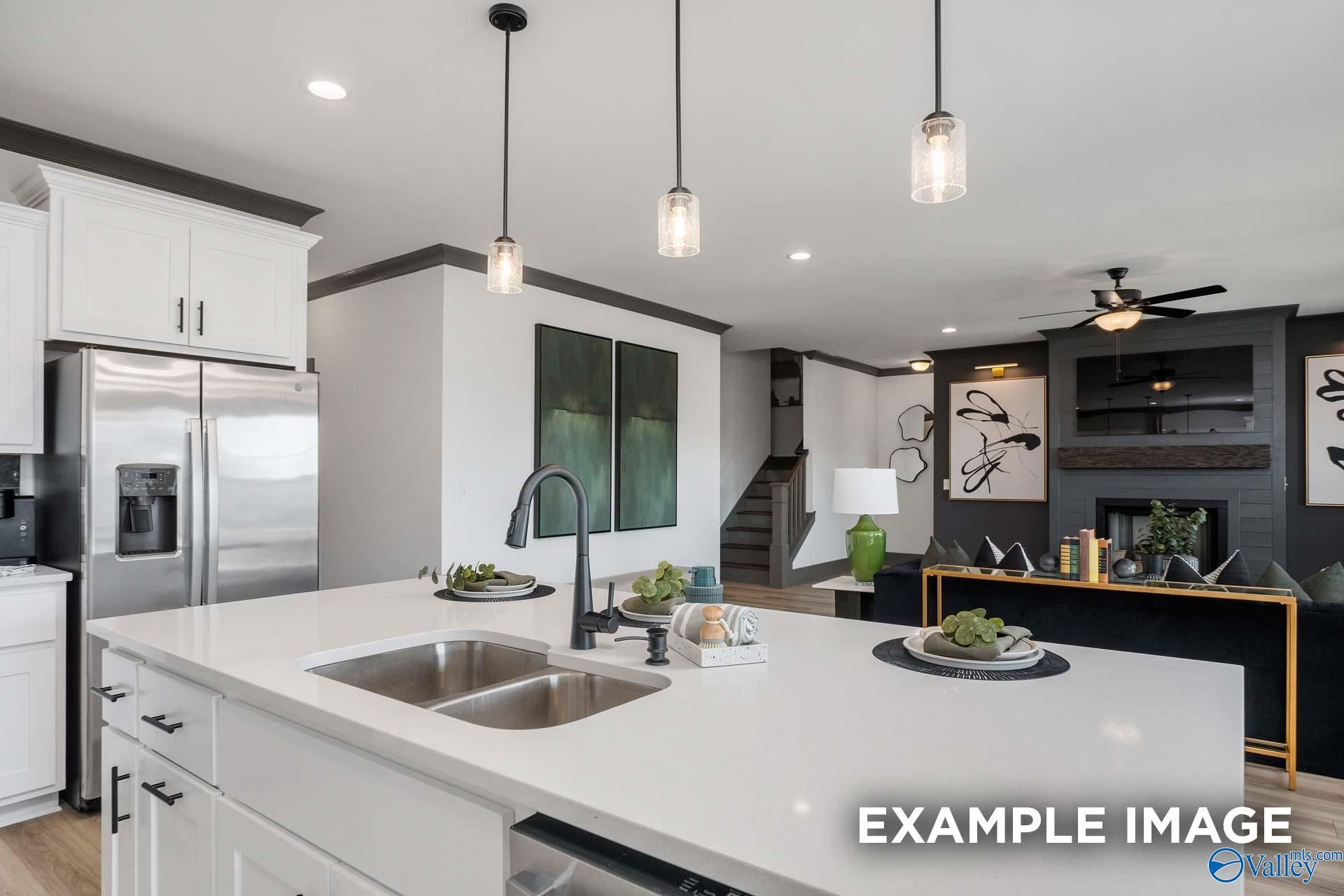 Modern open-concept kitchen with white cabinets, stainless fridge, island sink, and pendant lights in Davidson Homes The Rockford B, Madison, AL