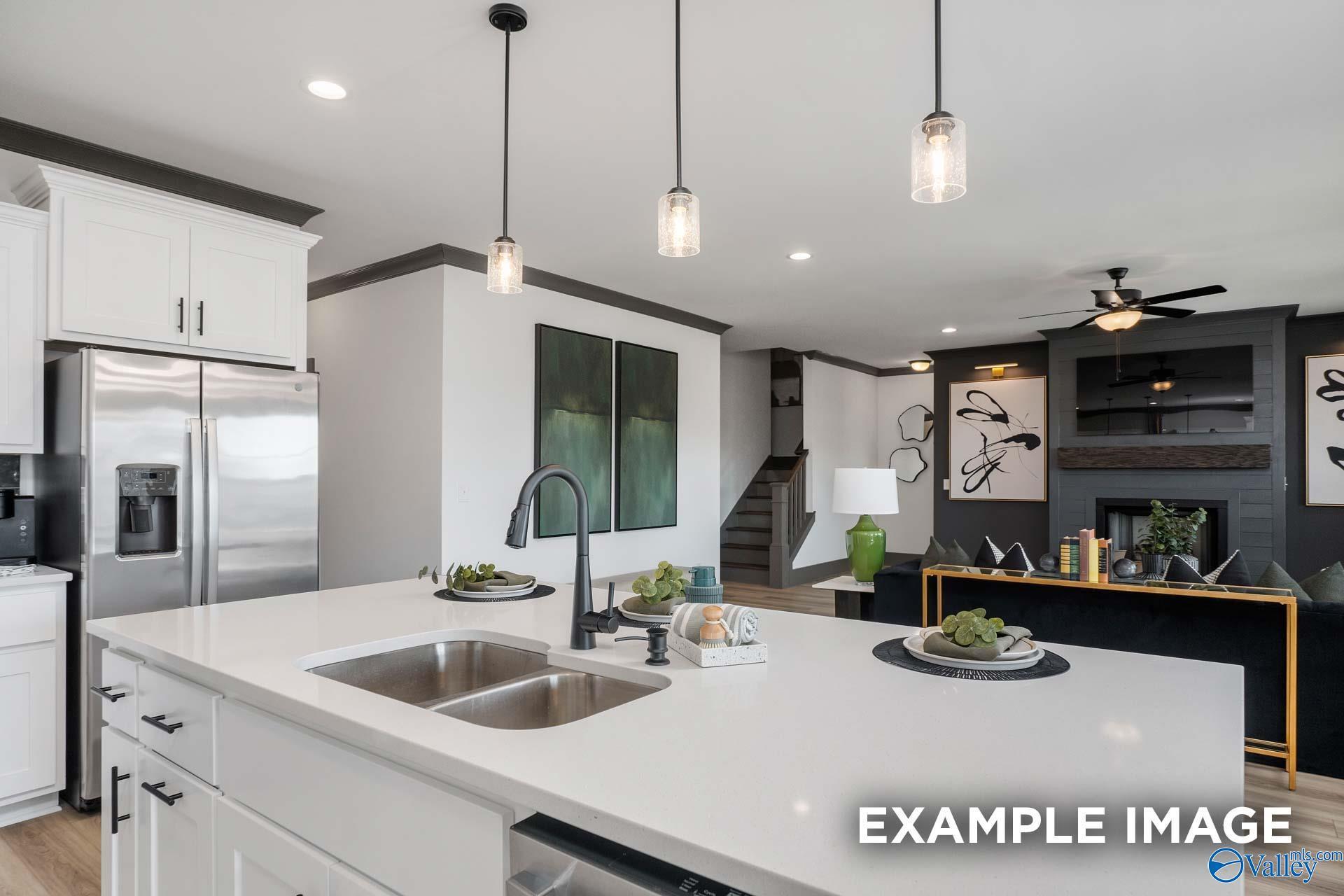 Modern open-concept kitchen with white cabinets, stainless fridge, island sink, and pendant lights in Davidson Homes The Rockford B, Madison, AL