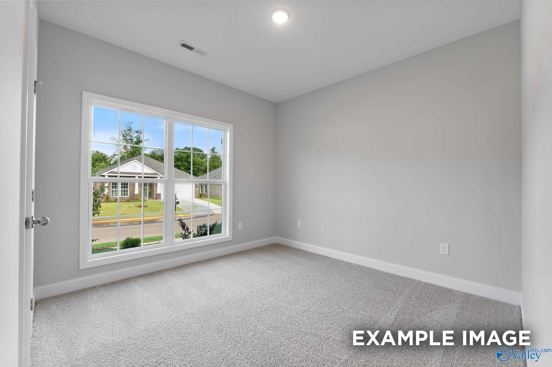 Empty bedroom with light gray walls, carpet floor, and large window view of yard in Davidson Homes The Franklin C, Athens, AL