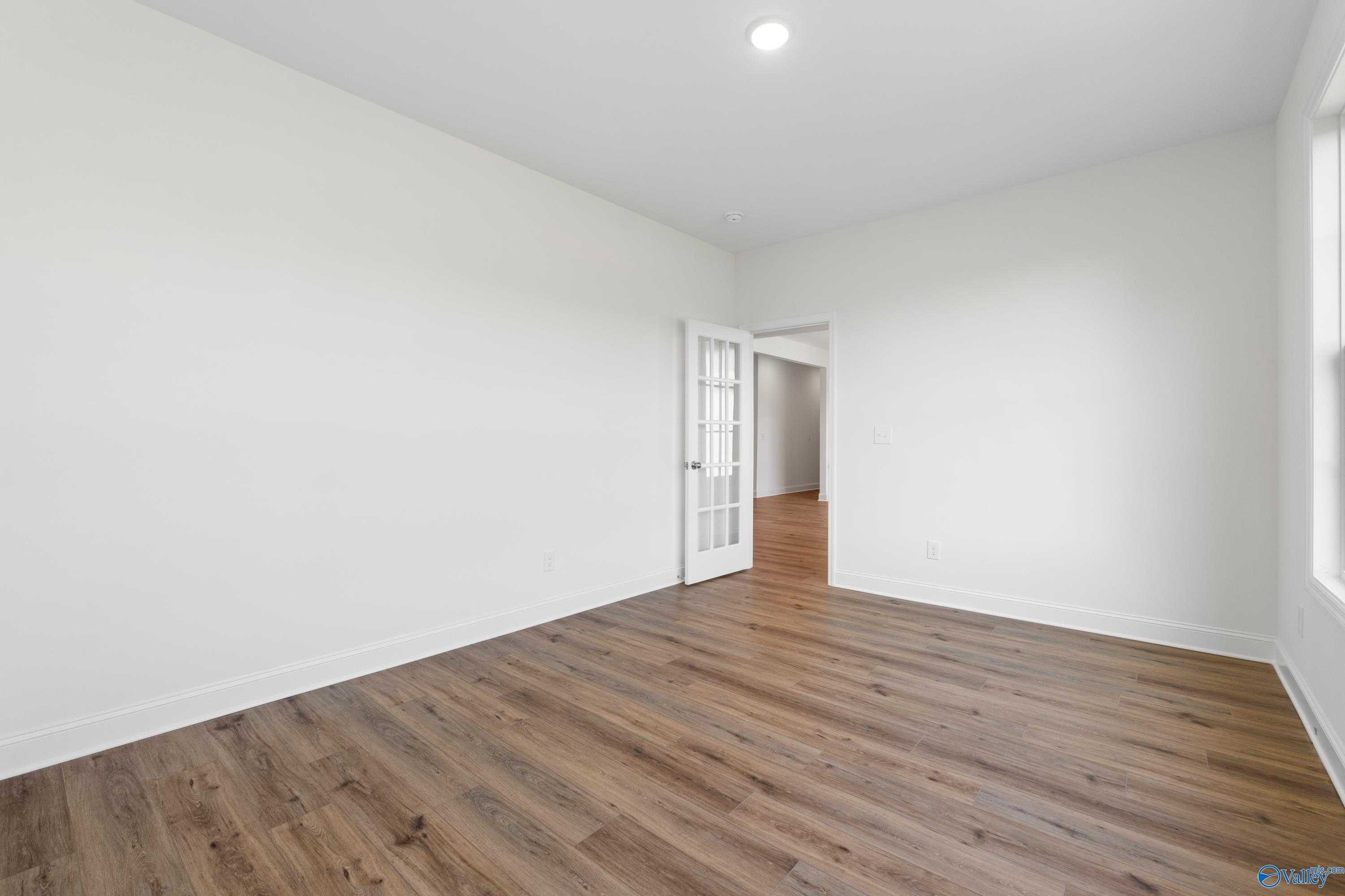 Bright secondary bedroom with light oak hardwood floors, white walls, French doors, and large window in Davidson Homes The Oxford, Harvest AL