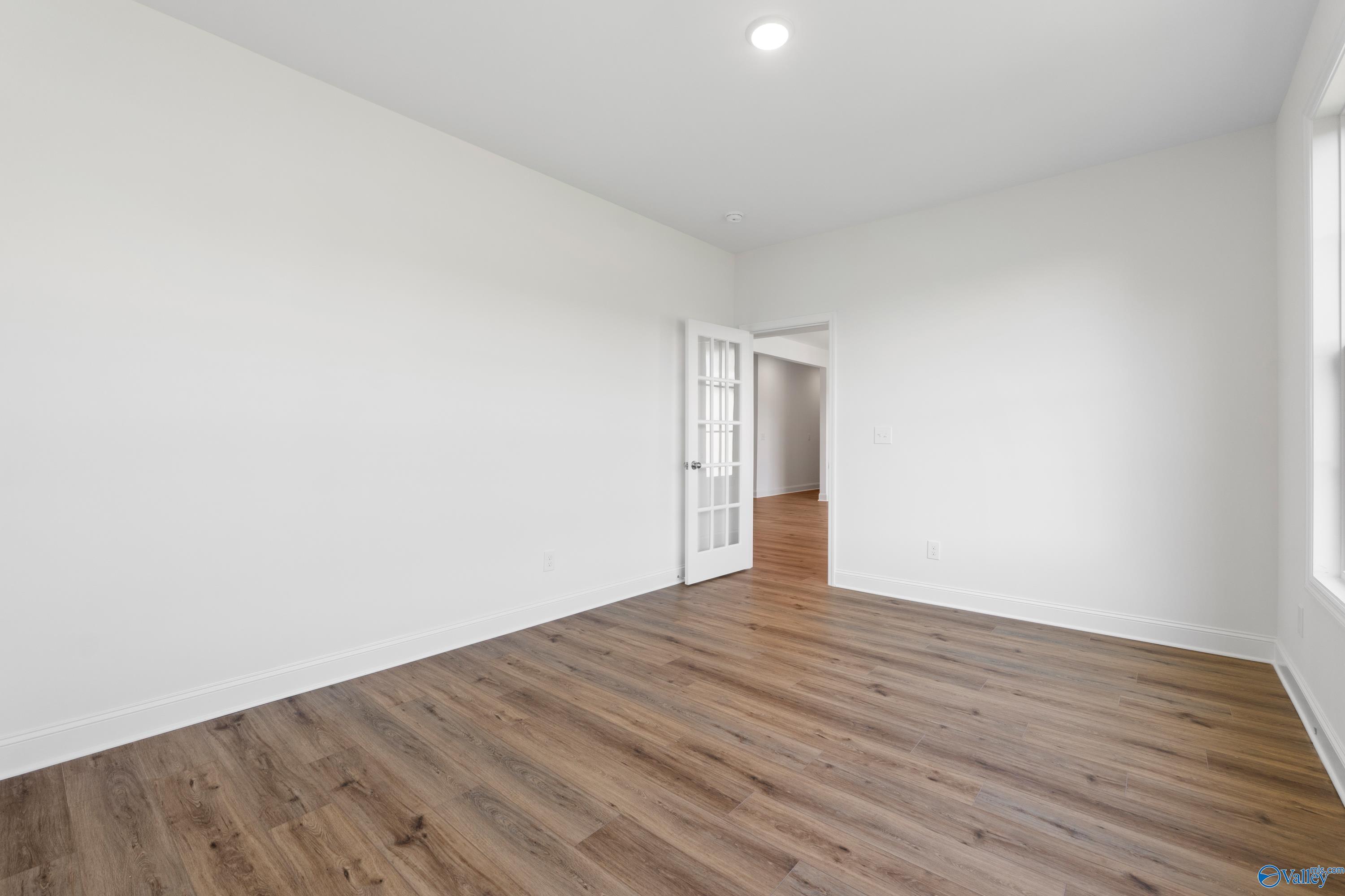 Bright secondary bedroom with light oak hardwood floors, white walls, French doors, and large window in Davidson Homes The Oxford, Harvest AL
