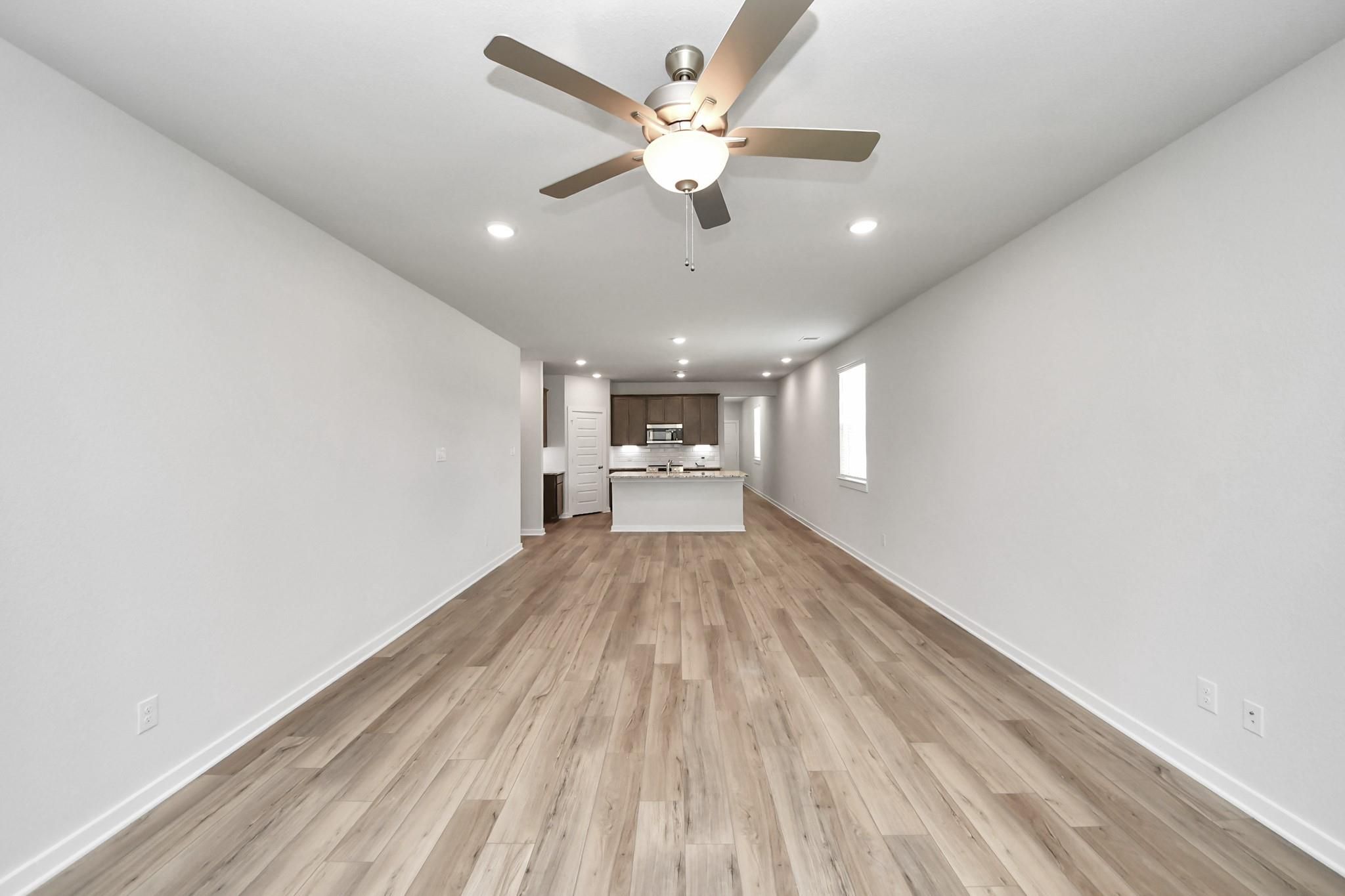 Open-concept living room and kitchen with wood-look flooring in The Sabine E floor plan at Liberty Estates, Cleveland, TX.