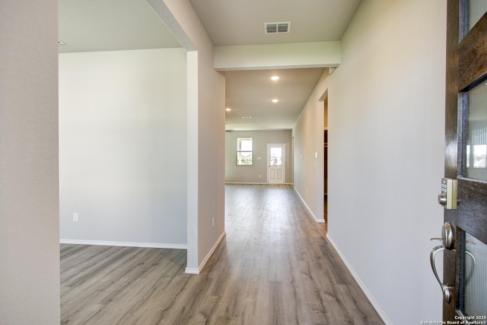 Bright entry hallway with light oak floors, white walls, and glass-paneled front door in Davidson Homes Douglas G, Comanche Ridge, San Antonio