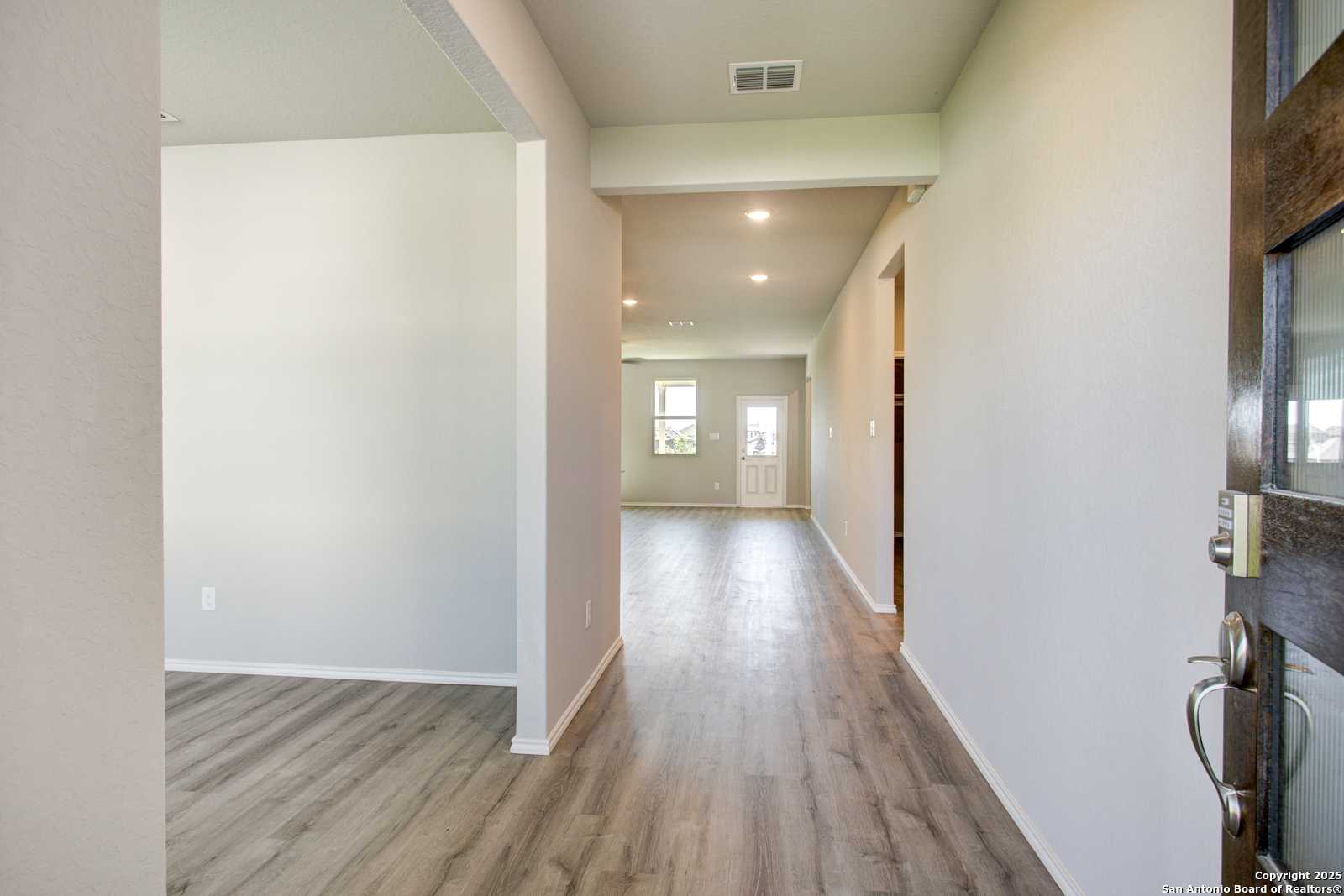 Bright entry hallway with light oak floors, white walls, and glass-paneled front door in Davidson Homes Douglas G, Comanche Ridge, San Antonio