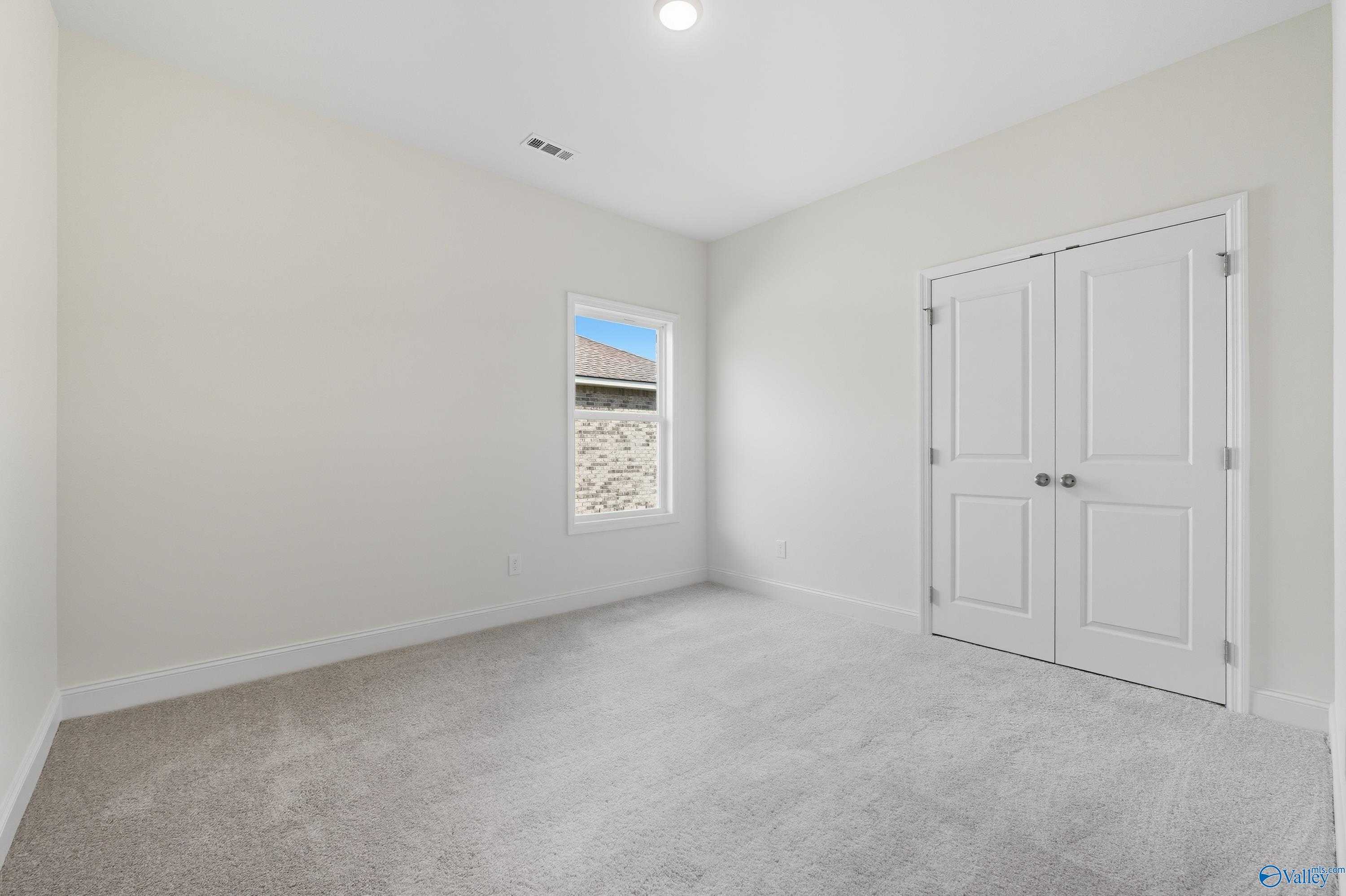 Bright bedroom with light walls, gray carpet, large window, and double closet doors in Davidson Homes The Everett, Meridianville, AL