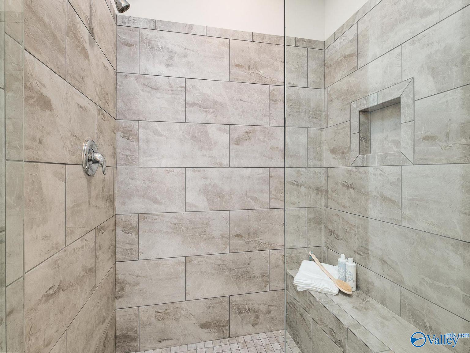 Modern walk-in shower with gray porcelain tile, glass enclosure, built-in bench, and niche in Davidson Homes The Everett, Toney, Alabama