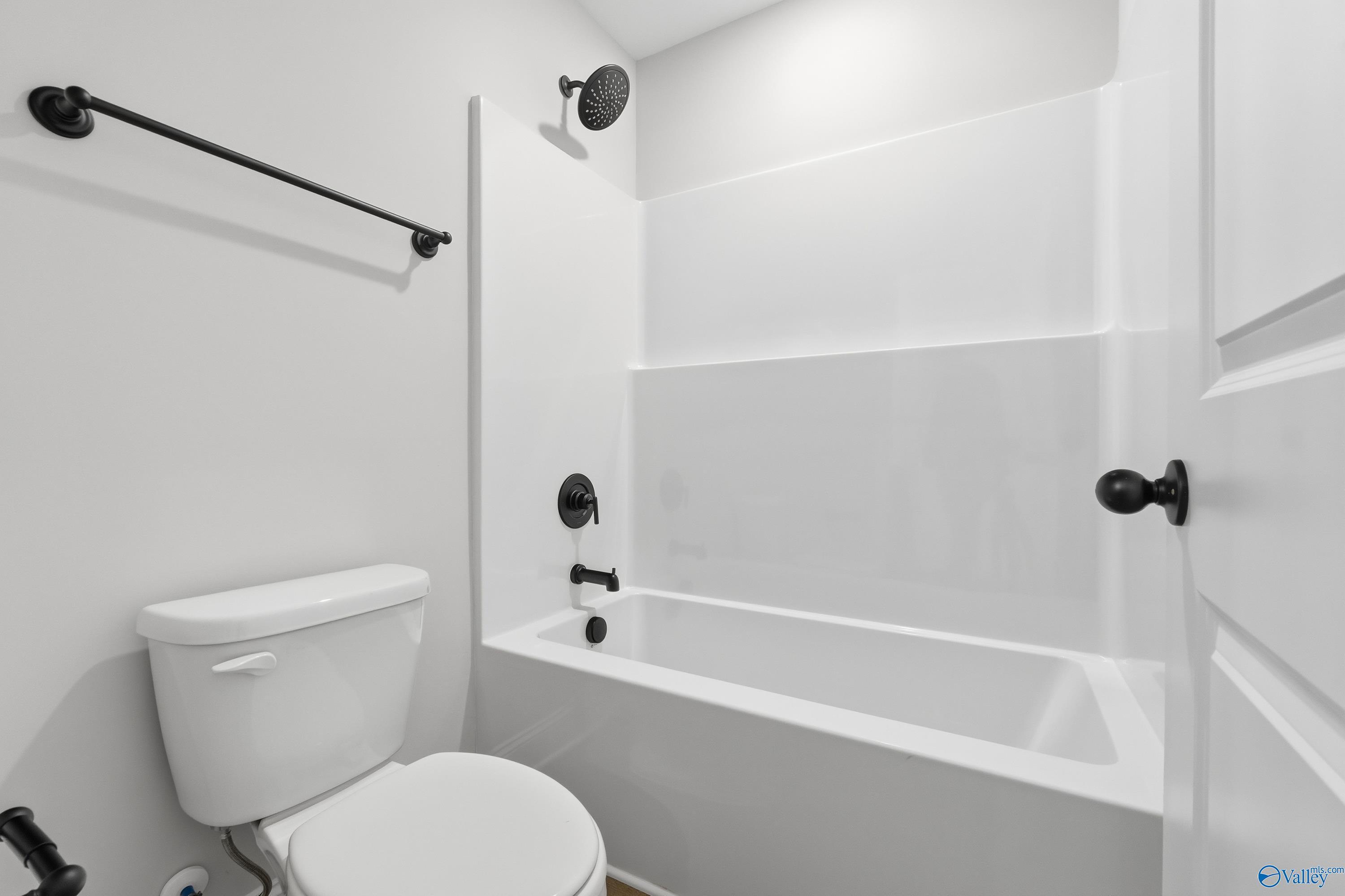 Modern white bathtub-shower combo with black fixtures and tiled surround in The Chelsea C bathroom, Harvest, Alabama