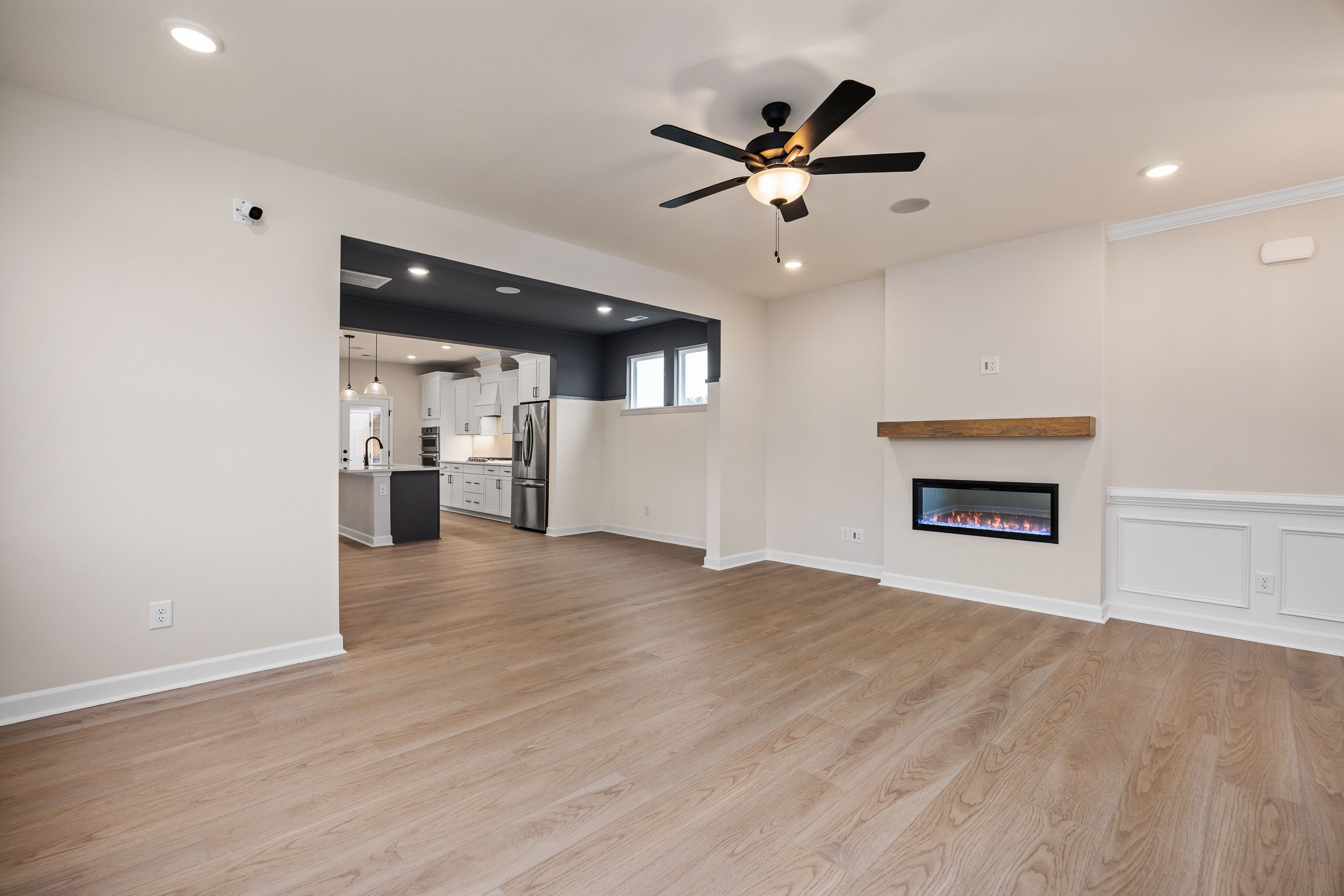 Open-concept living room at Forestville Yard in Knightdale NC with hardwood floors, gas fireplace mantel, ceiling fans, and adjacent kitchen