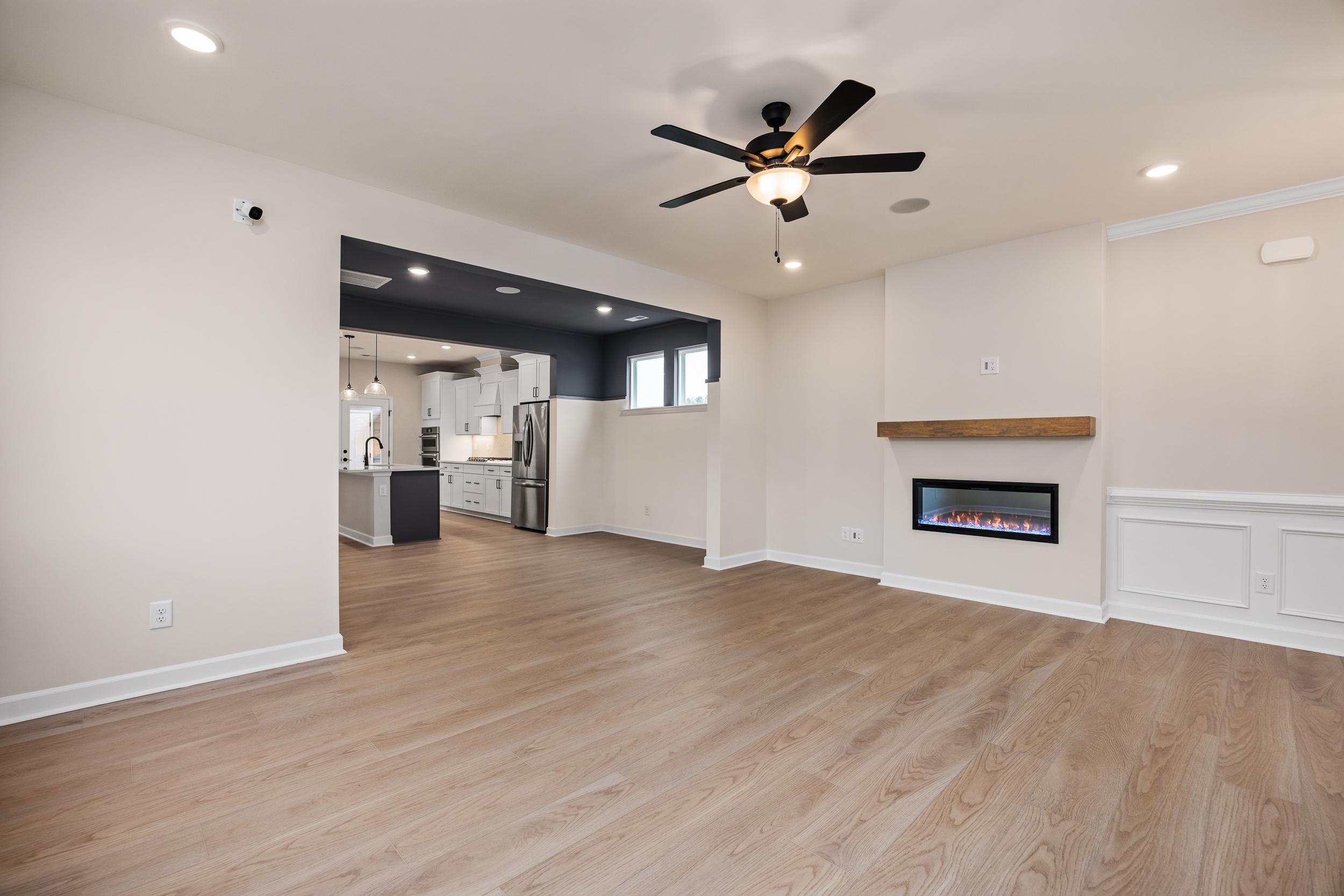 Open-concept living room at Forestville Yard in Knightdale NC with hardwood floors, gas fireplace mantel, ceiling fans, and adjacent kitchen