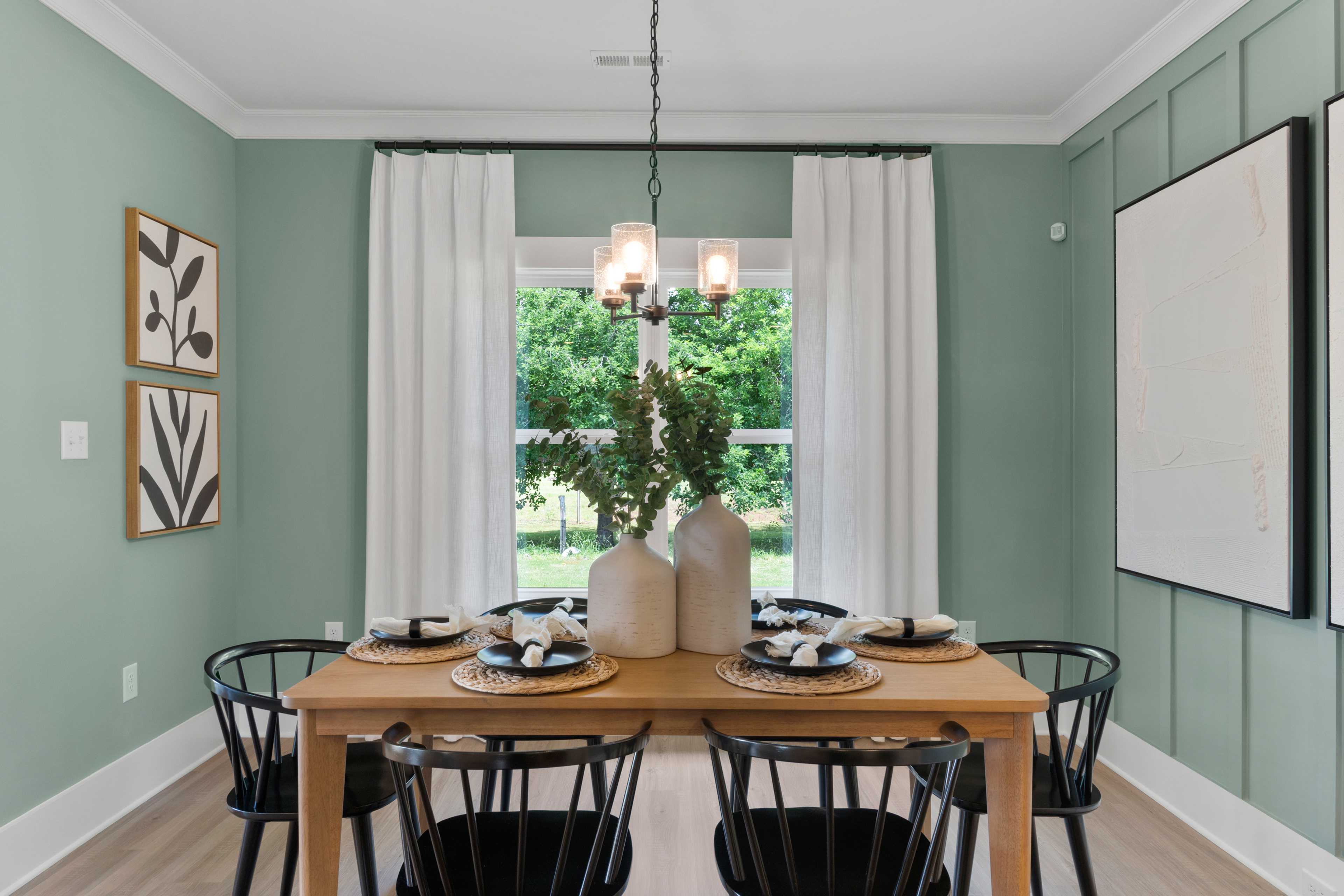 Cozy dining room at Hollon Meadow in Decatur AL with sage green walls, wooden table, black chairs, chandelier, and large windows