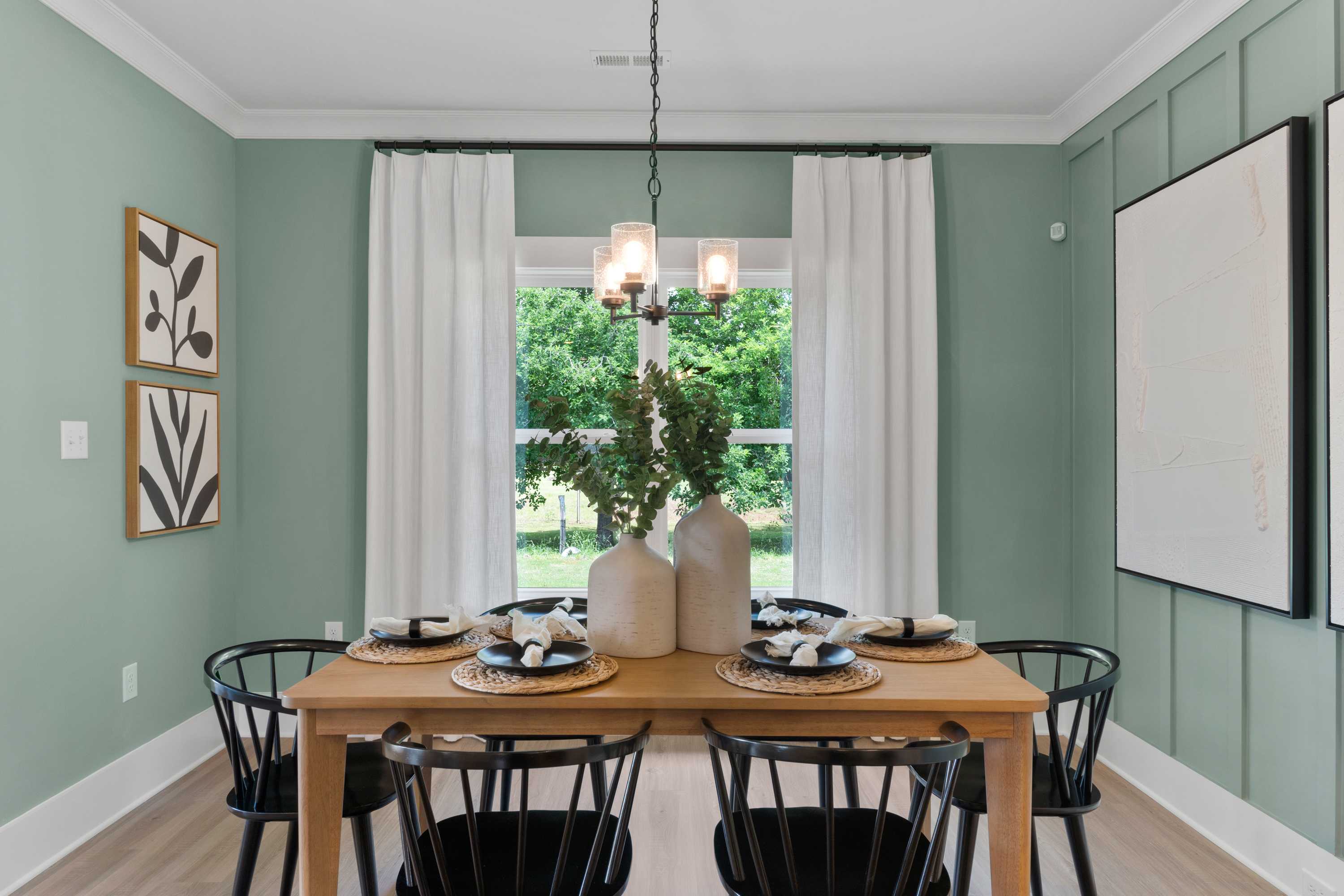 Cozy dining room at Hollon Meadow in Decatur AL with sage green walls, wooden table, black chairs, chandelier, and large windows