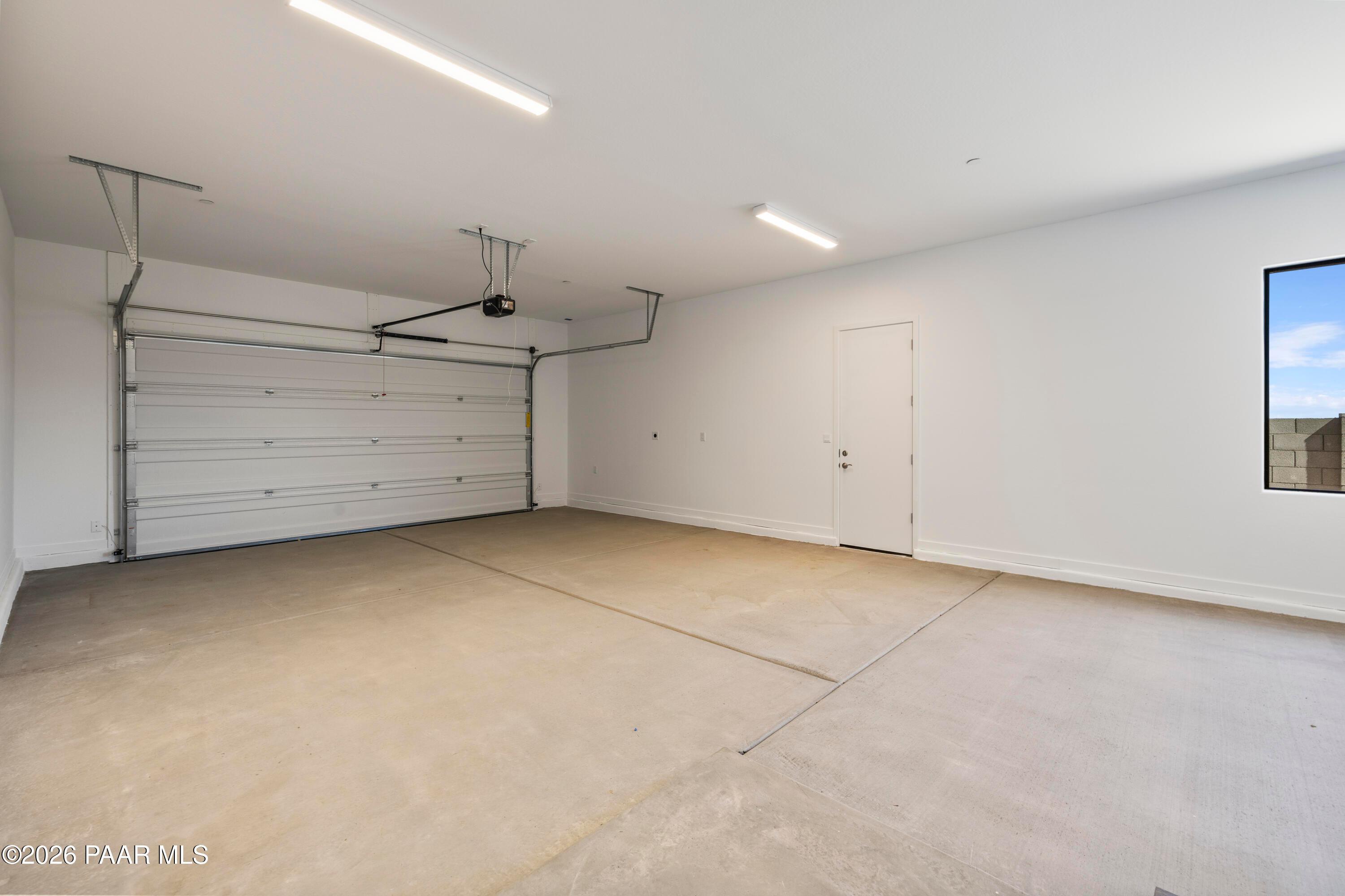 Spacious three-car garage with open doors, white walls, and concrete floor in Davidson Homes The Soleil E, Hidden Hills, Prescott, Arizona
