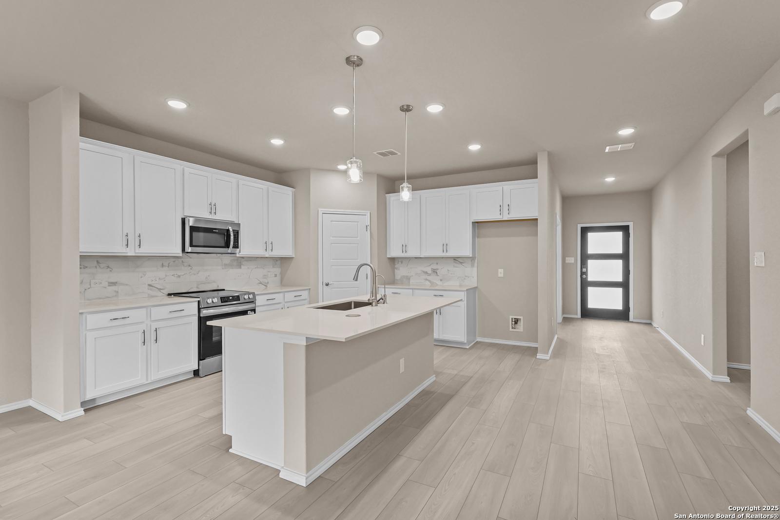 Bright open-concept kitchen with white shaker cabinets, quartz island, stainless appliances in Davidson Homes Douglas G, San Antonio