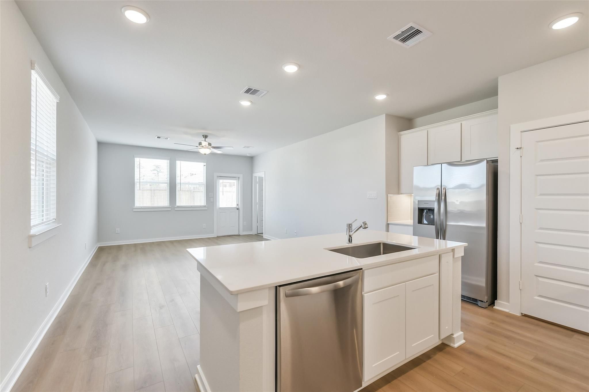 Modern open-concept kitchen with white island sink, stainless steel fridge, and hardwood floors in Davidson Homes The Colorado F, Cleveland, Texas