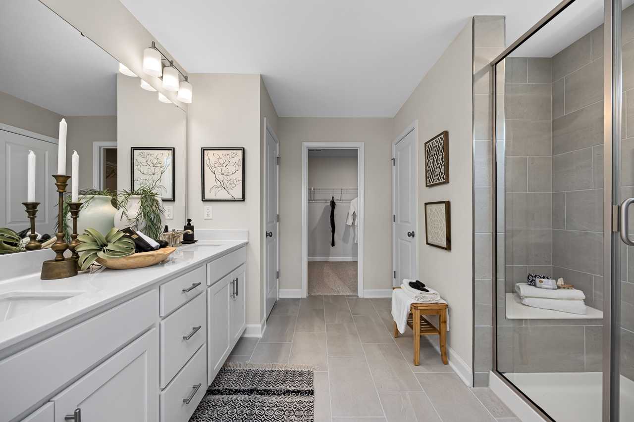 Spacious primary bathroom at Wellers Knoll in Lillington NC with double white vanity, frameless glass shower, and walk-in closet