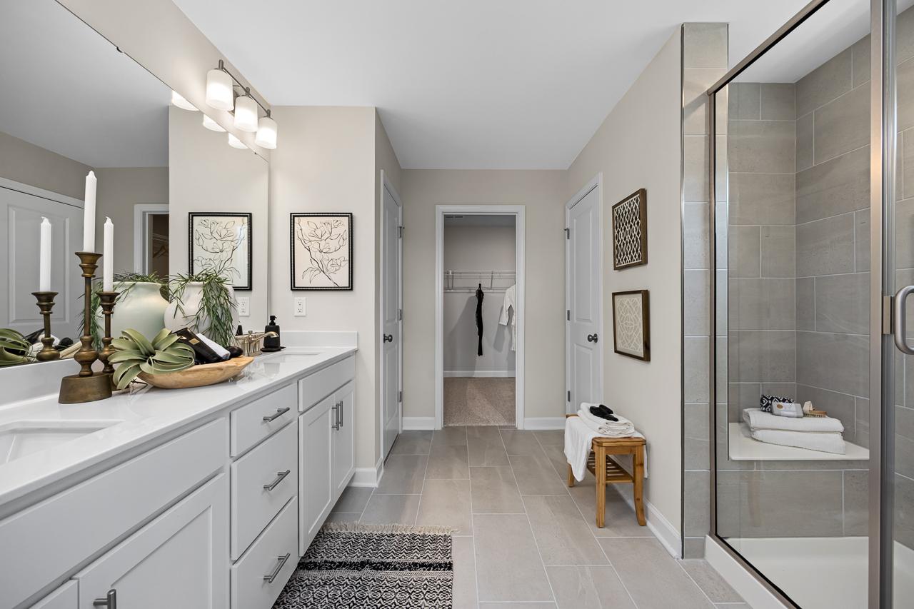 Spacious primary bathroom at Wellers Knoll in Lillington NC with double white vanity, frameless glass shower, and walk-in closet
