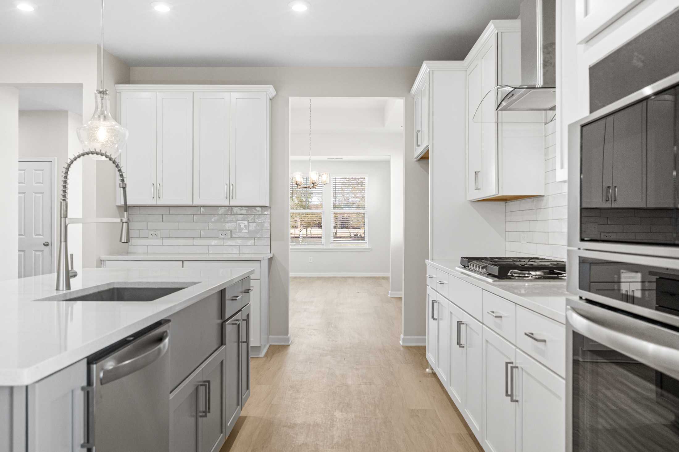 Spacious kitchen in The Glenwood A showcasing white cabinets, gray island with farmhouse sink, stainless steel appliances, and open hallway view