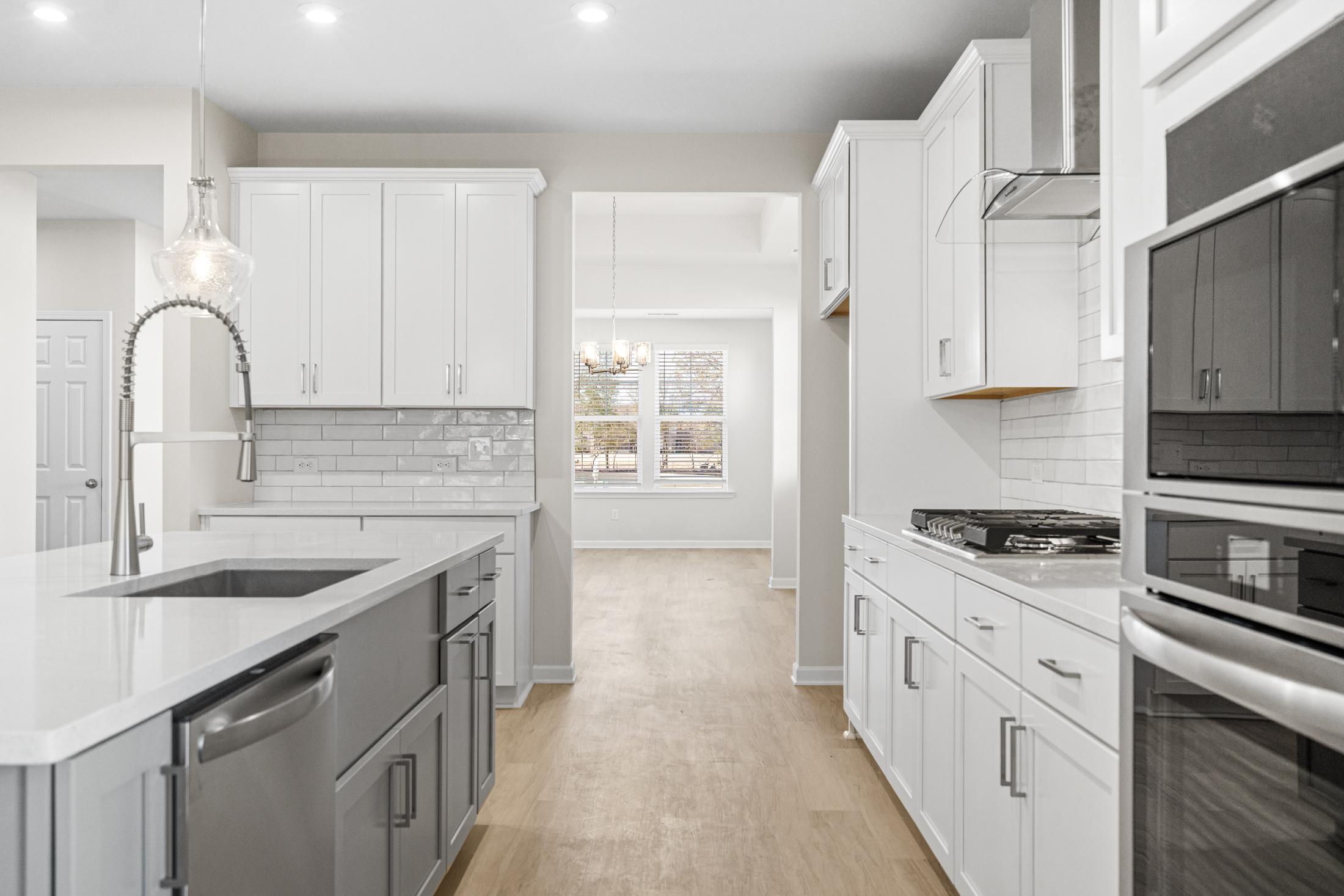 Spacious kitchen in The Glenwood A showcasing white cabinets, gray island with farmhouse sink, stainless steel appliances, and open hallway view
