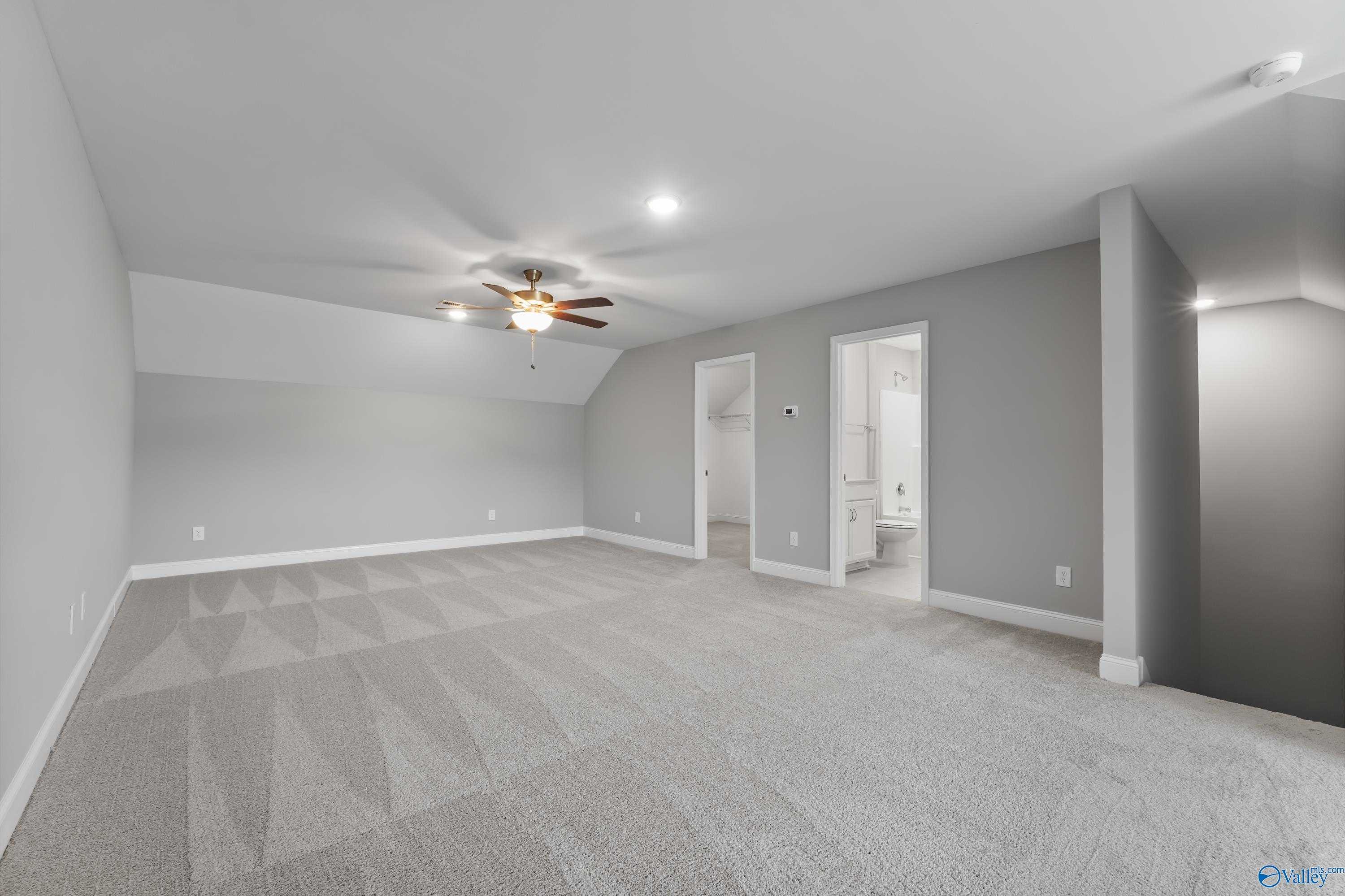 Spacious bonus room with vaulted ceiling, ceiling fan, gray carpet, and en-suite bath in Davidson Homes The Rockford, Harvest, AL