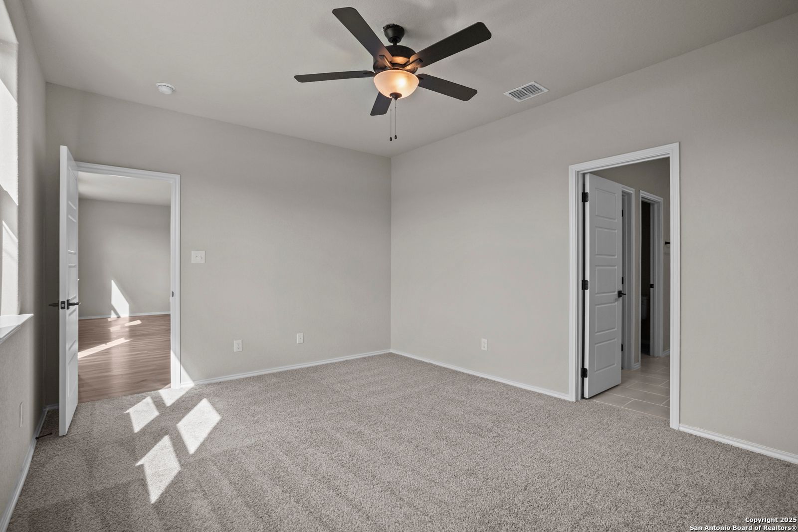 Spacious empty bedroom with ceiling fan, neutral gray walls, and carpeted floor in Davidson Homes The Douglas F, San Antonio