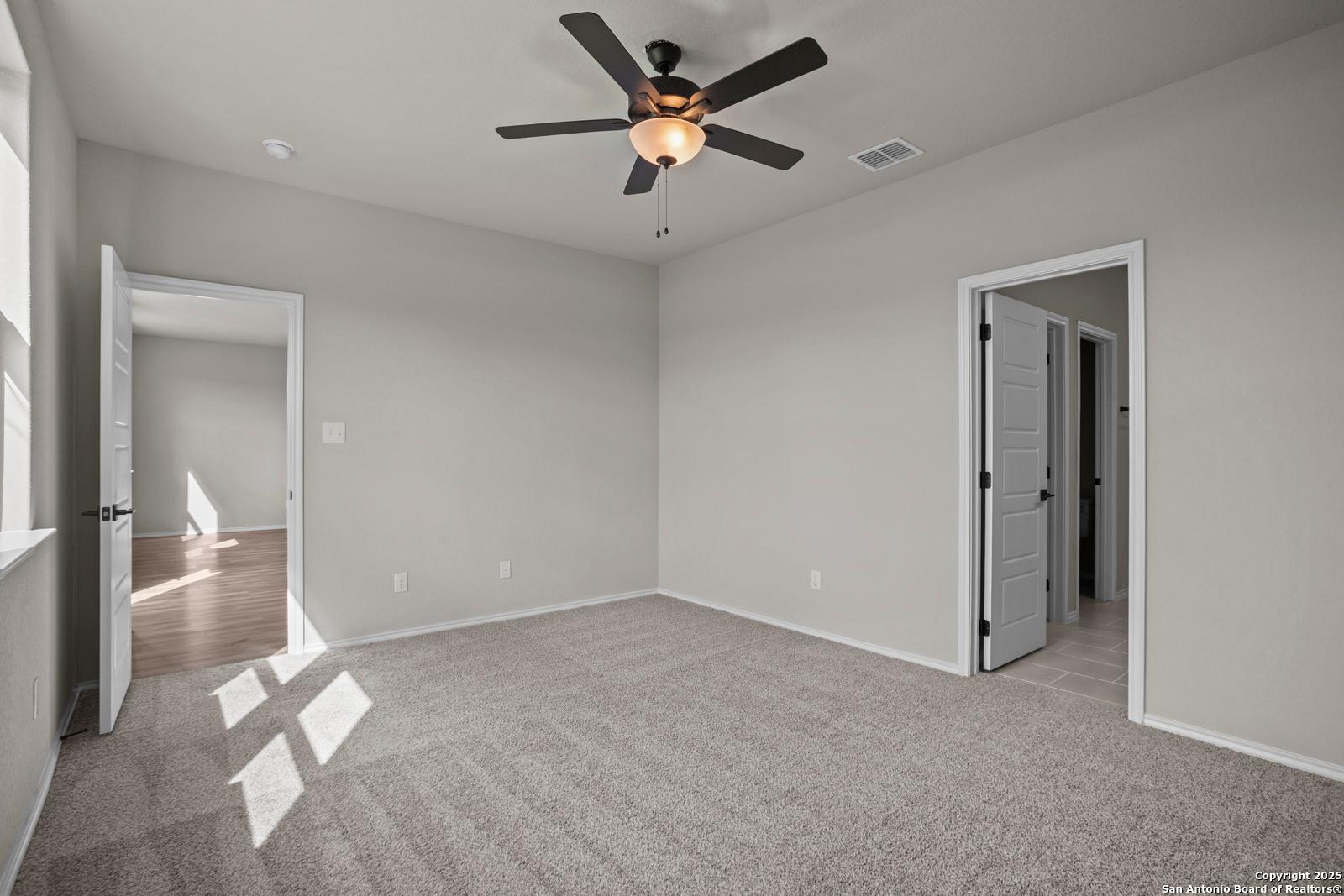 Spacious empty bedroom with ceiling fan, neutral gray walls, and carpeted floor in Davidson Homes The Douglas F, San Antonio